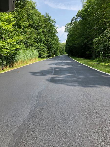 Paved road lined with trees under a blue sky.