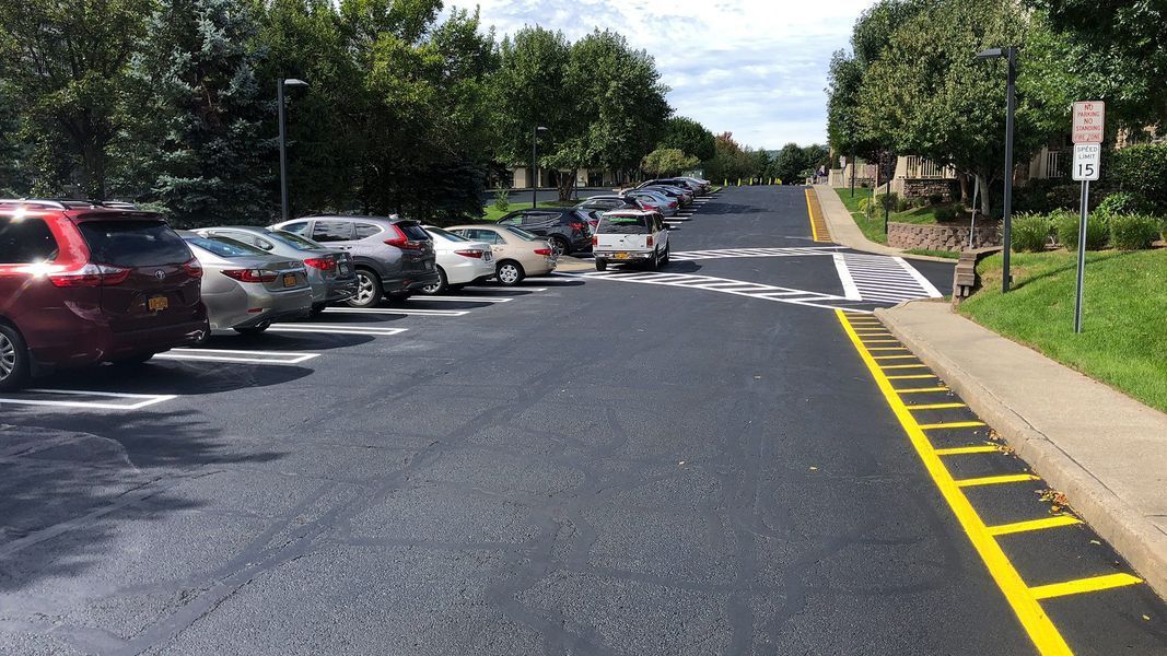 Asphalt parking lot with parked cars, crosswalk, and curb ramp leading uphill to a building.