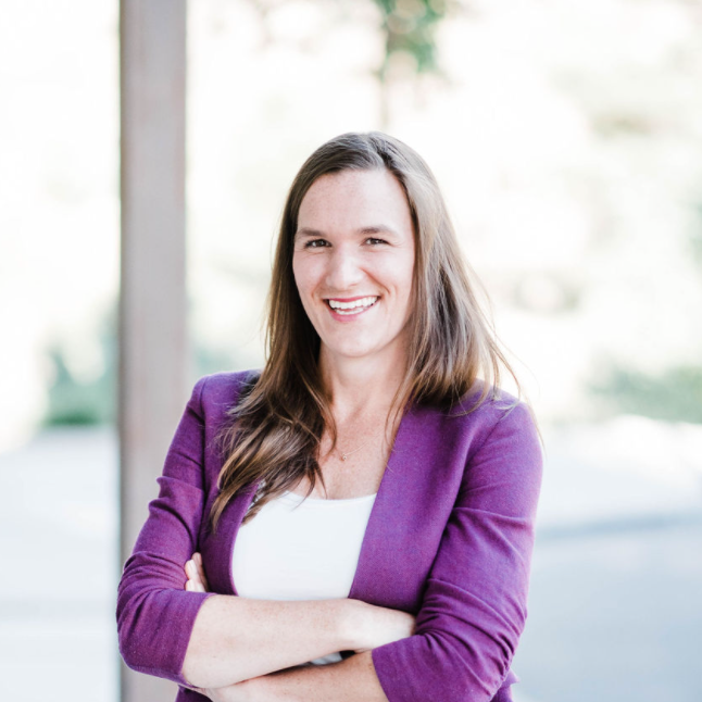 Smiling person in a purple cardigan with arms crossed against a bright background