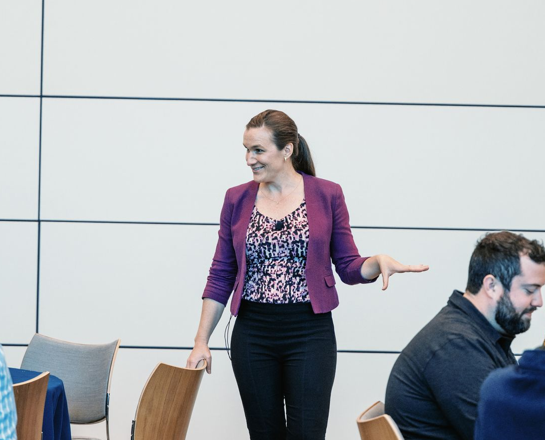 Woman in a purple blazer gesturing while speaking in a modern meeting room