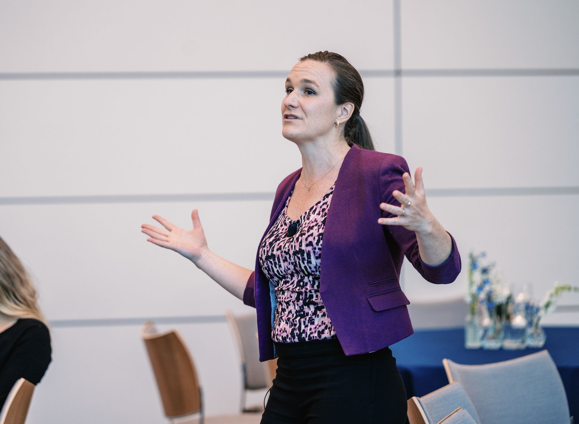 Woman in a purple blazer speaking with open hands in a conference room