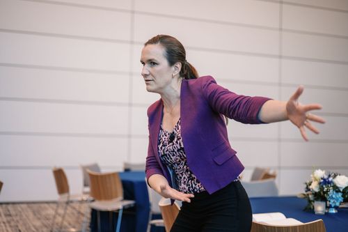 Woman in a purple blazer gesturing during a presentation in a conference room