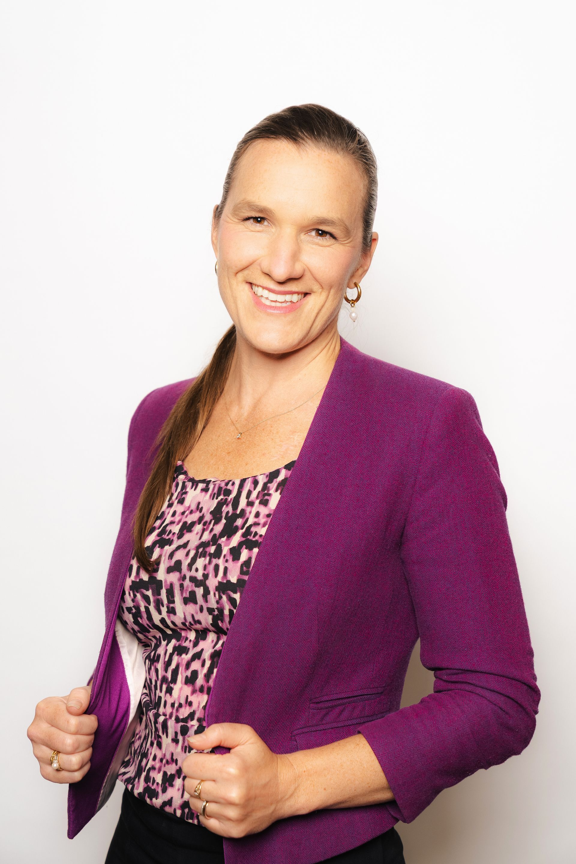 Smiling person in a purple blazer over a patterned top against a white background