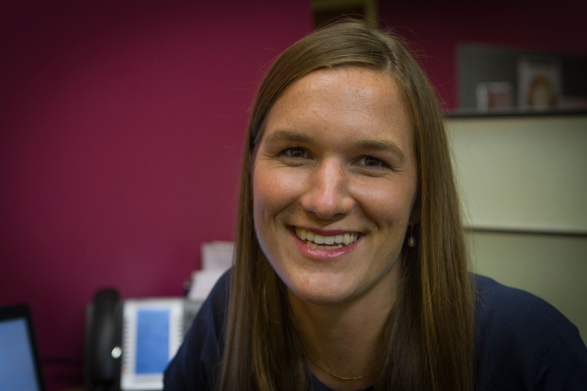 Smiling woman in an office with a magenta wall and a computer in the background