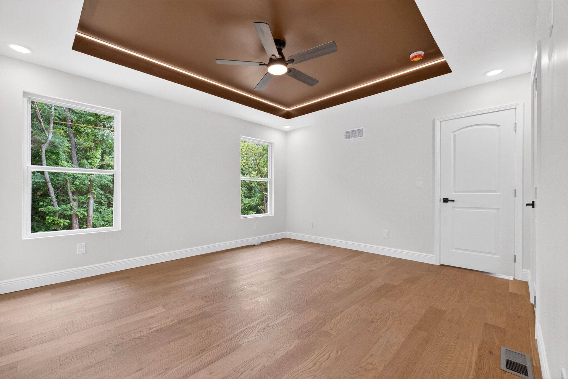 Empty white bedroom with hardwood floors, two windows, a ceiling fan, and a white door