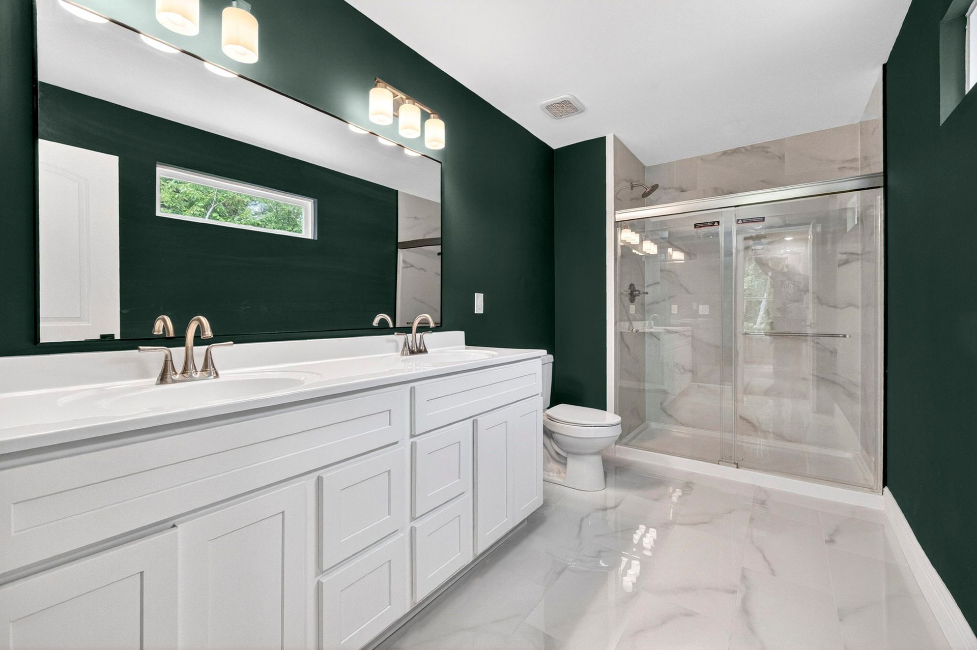 Modern bathroom with dark green walls, white vanity, large mirror, and glass shower enclosure