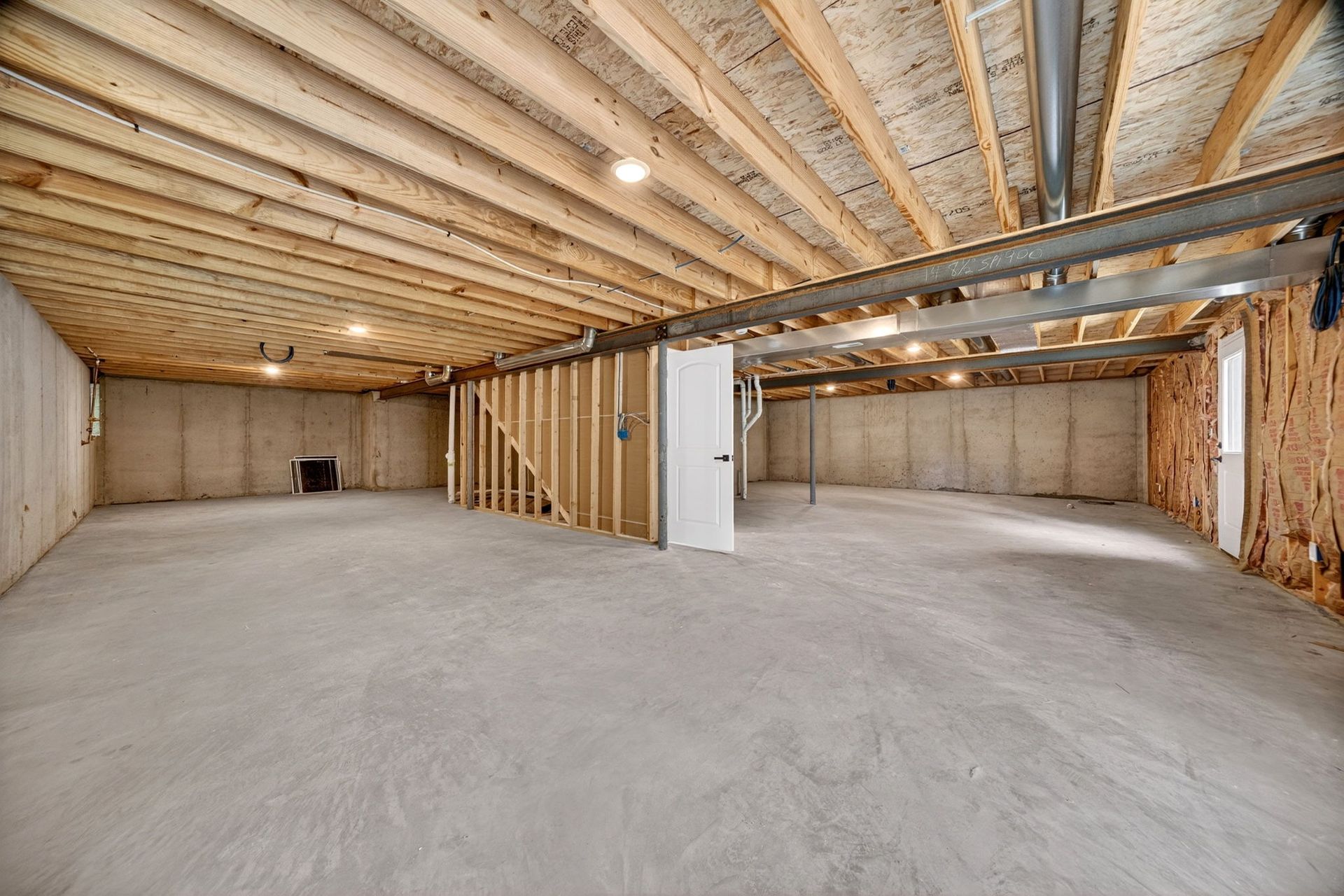 Unfinished basement with exposed beams, concrete floor, and framed interior walls under construction