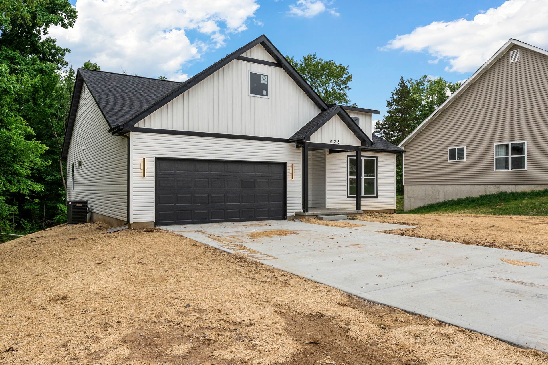 New white house with black garage doors and a concrete driveway under construction