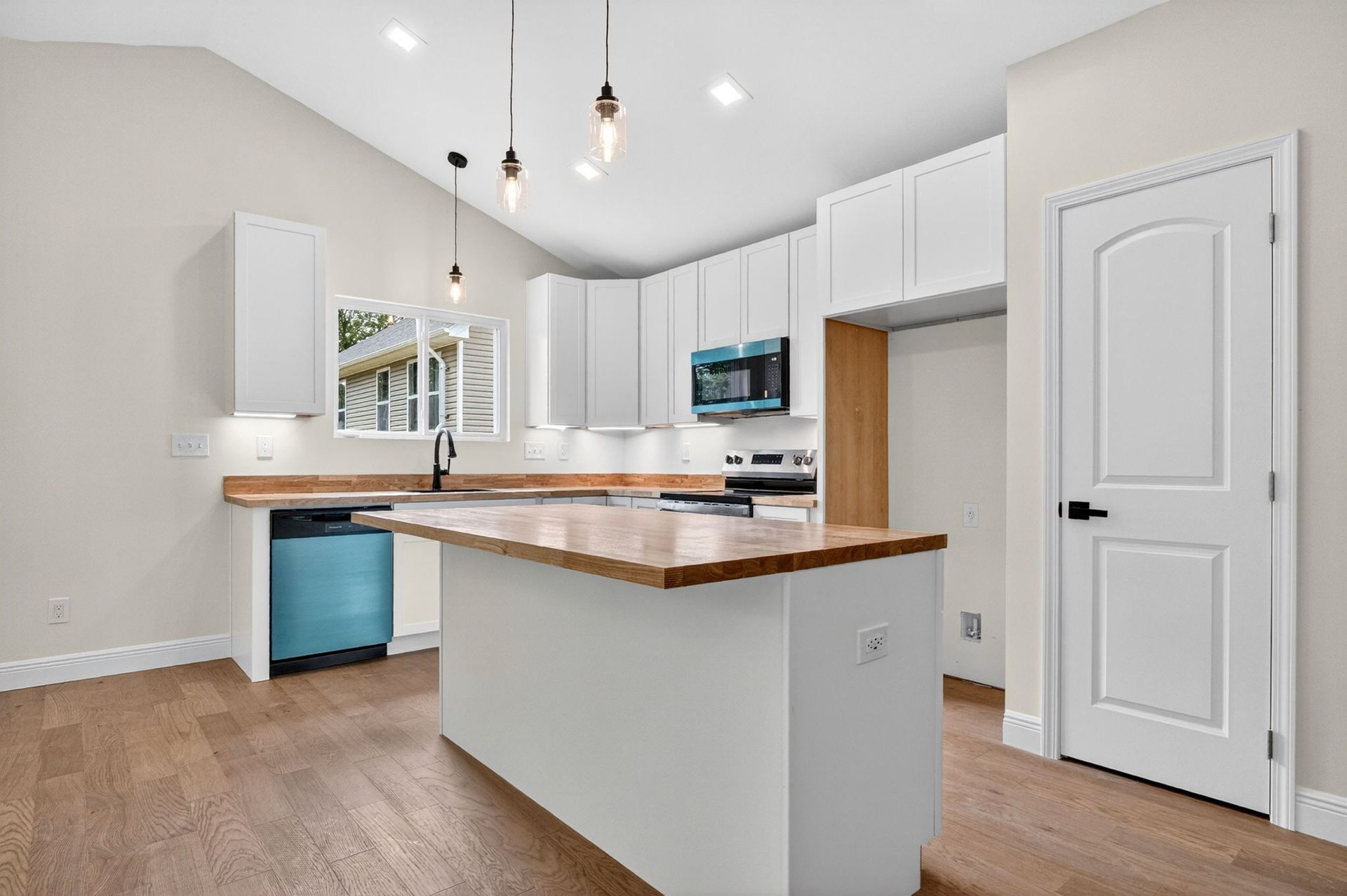 Bright modern kitchen with white cabinets, wooden countertops, pendant lights, and a central island.