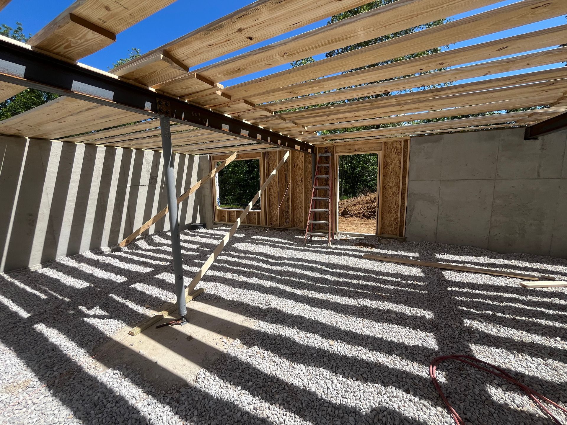 Interior of a unfinished building with exposed beams, concrete walls, and sunlight casting striped shadows on the floor.