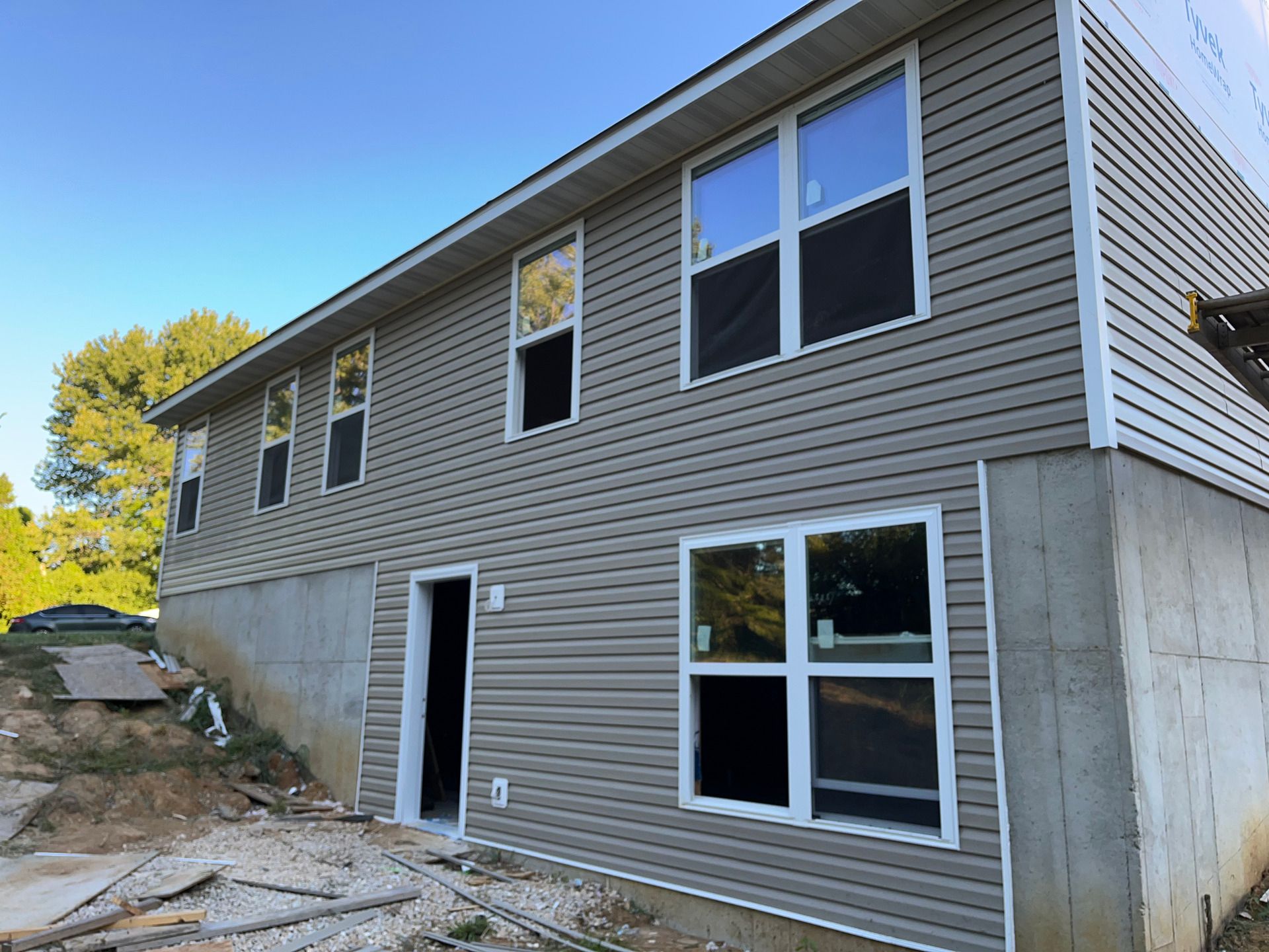 Two-story gray house exterior with unfinished concrete foundation and white-trimmed windows under a blue sky
