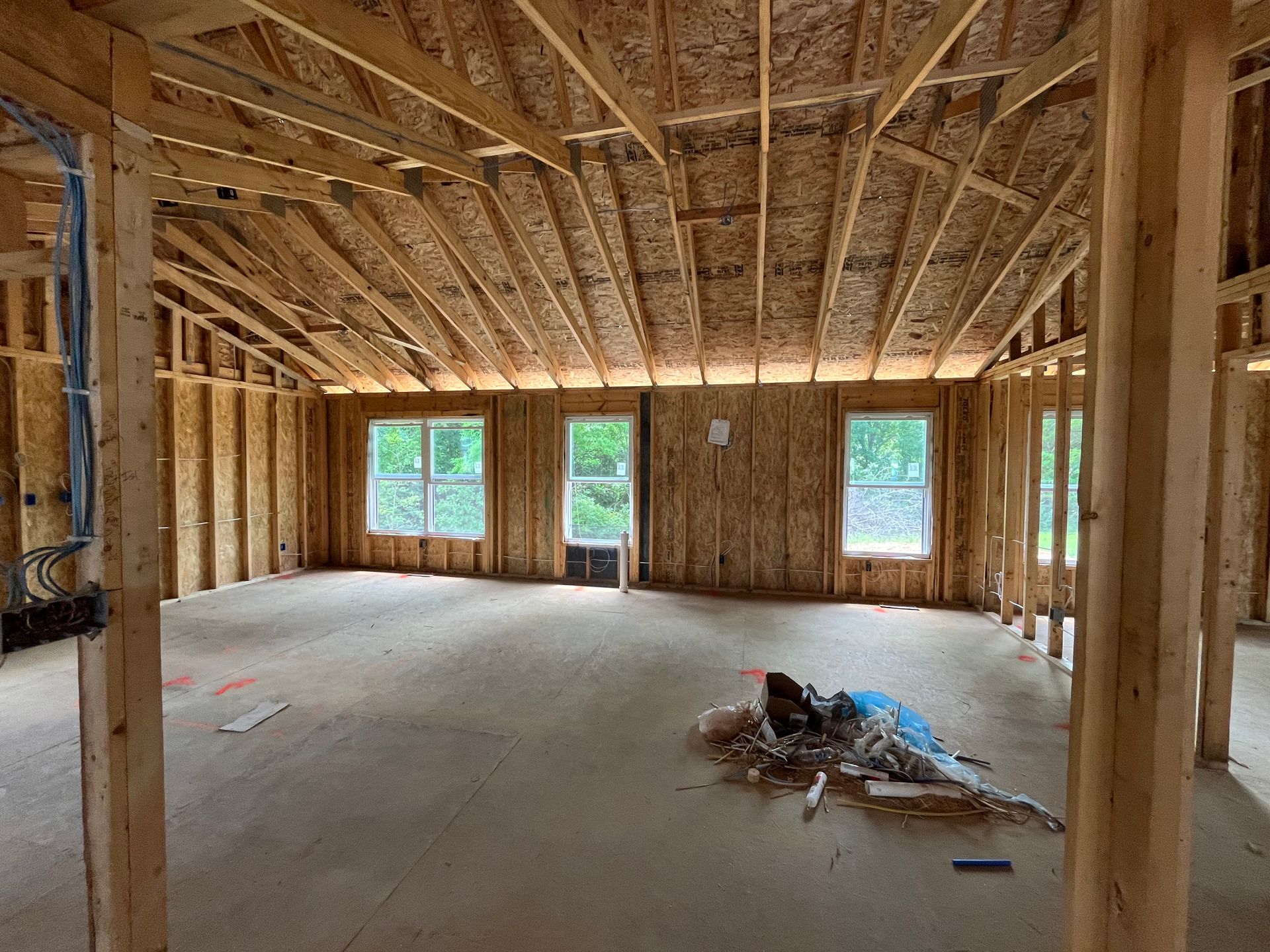 Unfinished house interior with exposed wood framing, concrete floor, and sunlight through windows