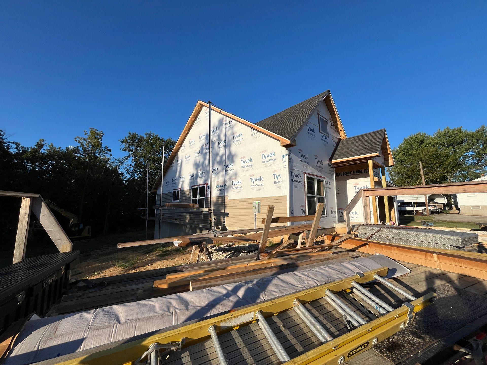 Partially built house with scaffolding, lumber, and construction materials in a yard under a clear blue sky