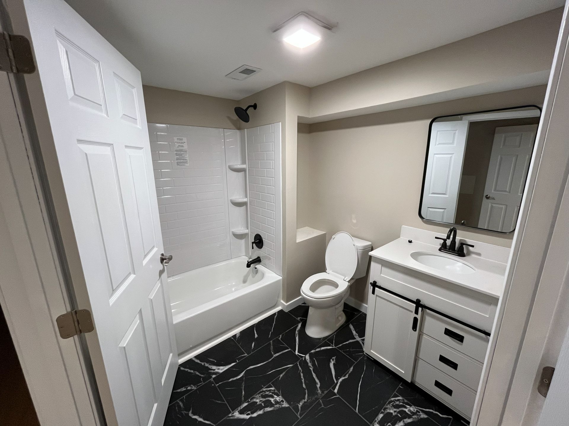 Small bathroom with white vanity, toilet, tub-shower, and black marble-look tile floor.