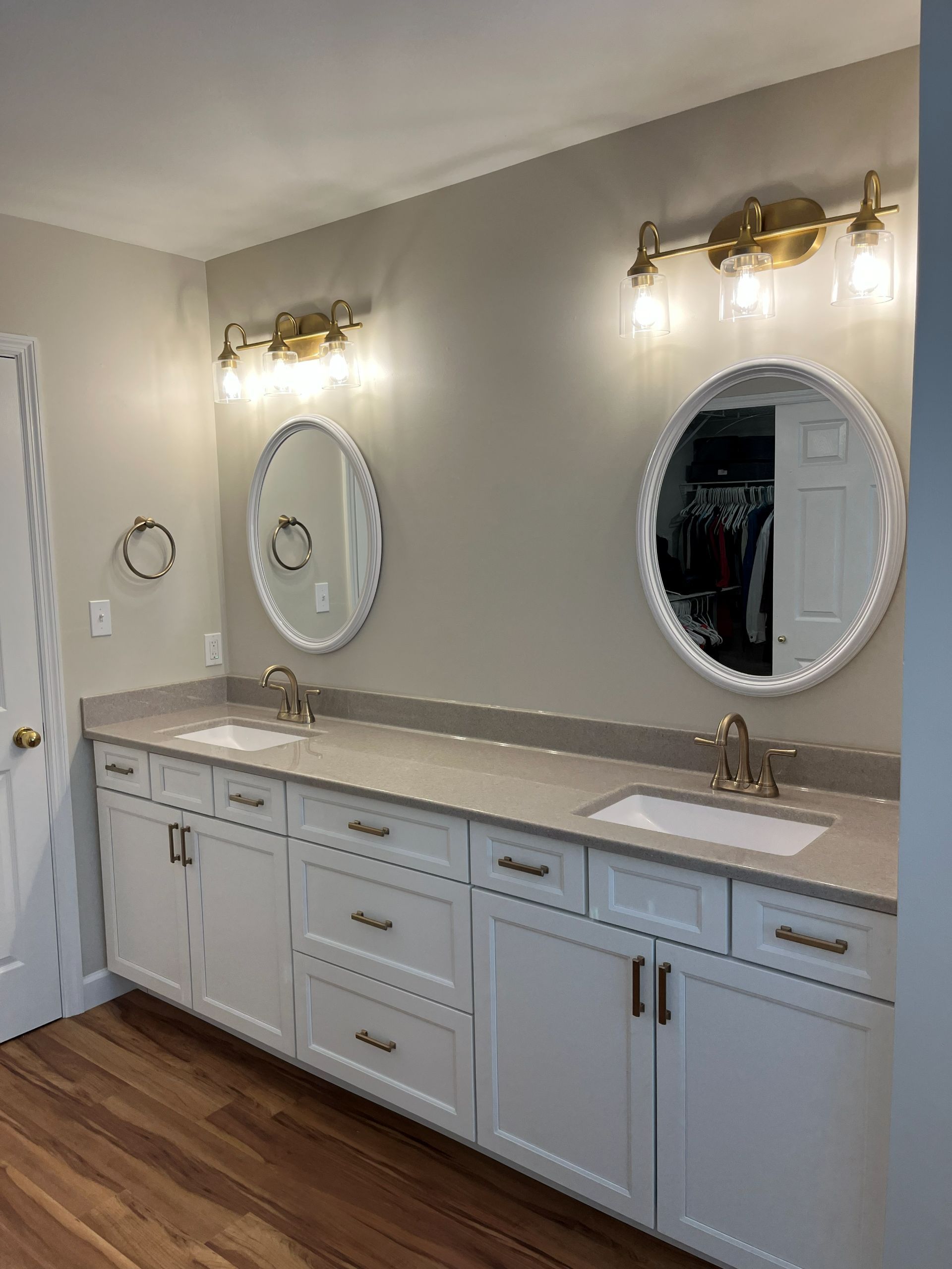 Spacious bathroom vanity with two oval mirrors, white cabinets, and brass wall sconces