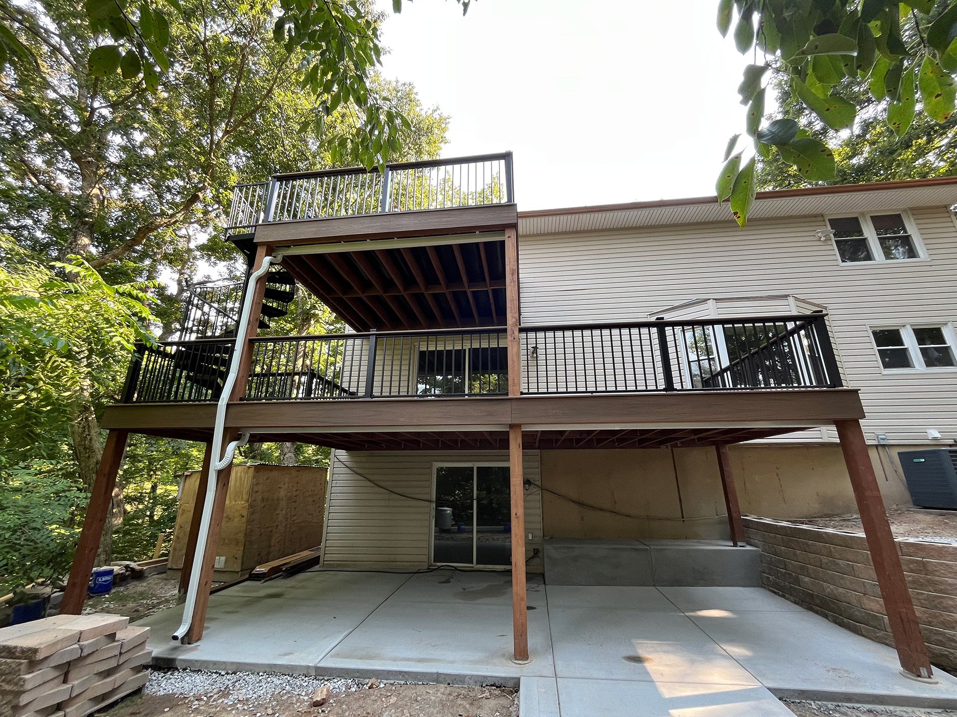 Backyard deck with stairs, upper and lower patios, and a house exterior under trees
