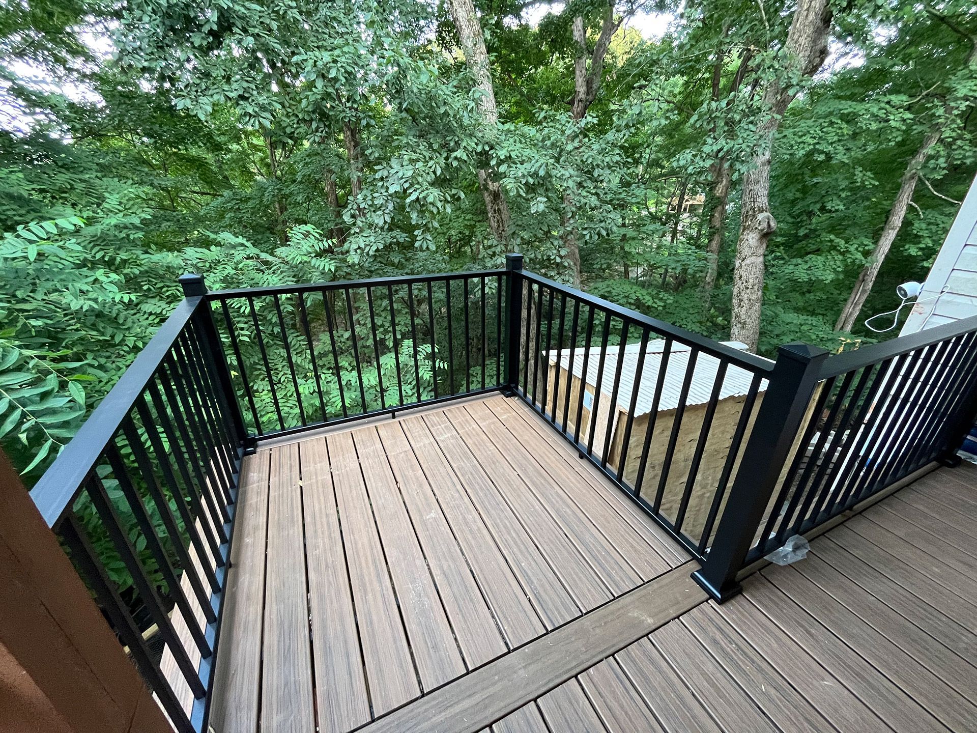 Small wooden deck with black railing overlooking a wooded area