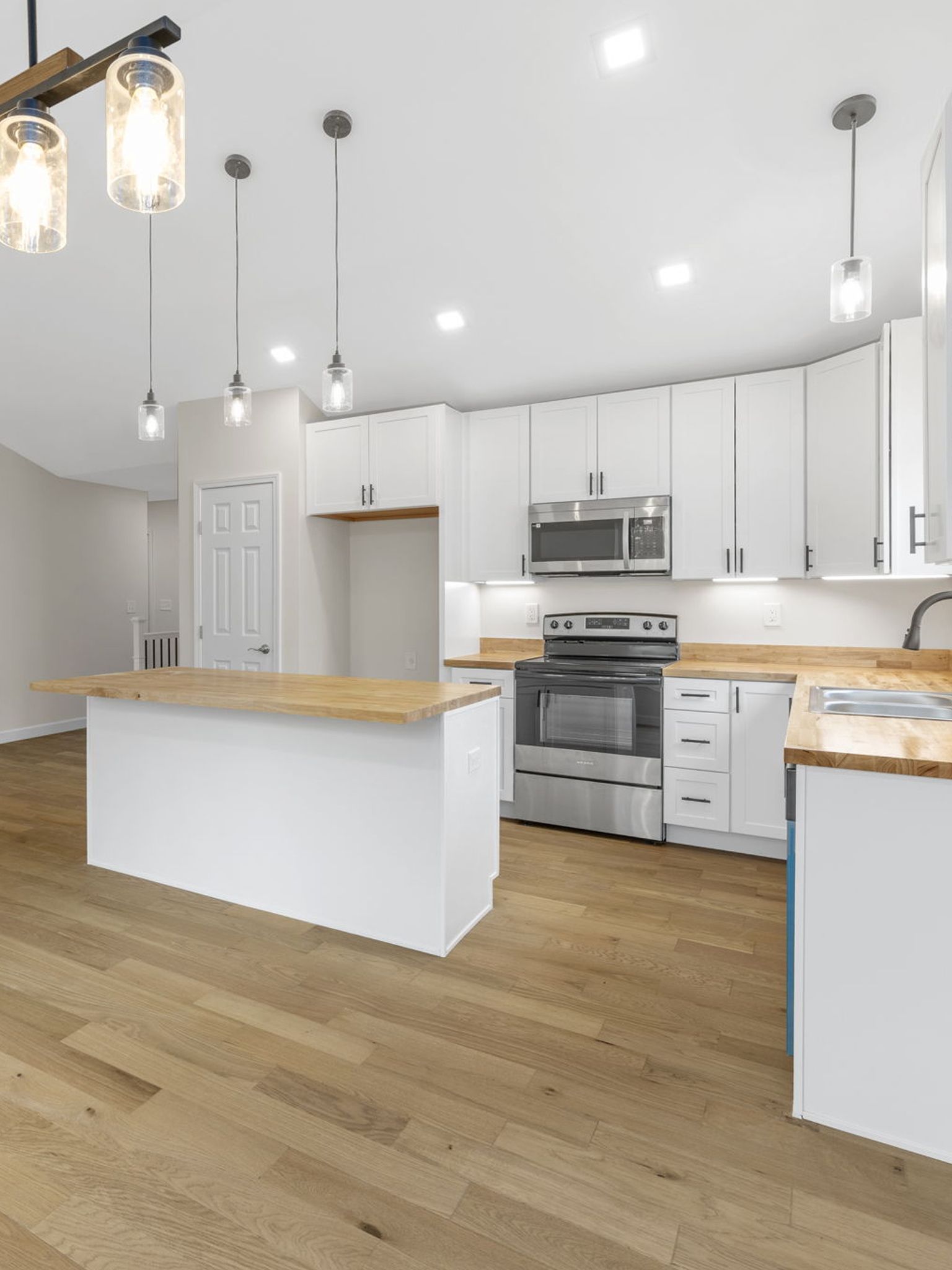 Bright modern kitchen with white cabinets, wood island, stainless appliances, and pendant lights