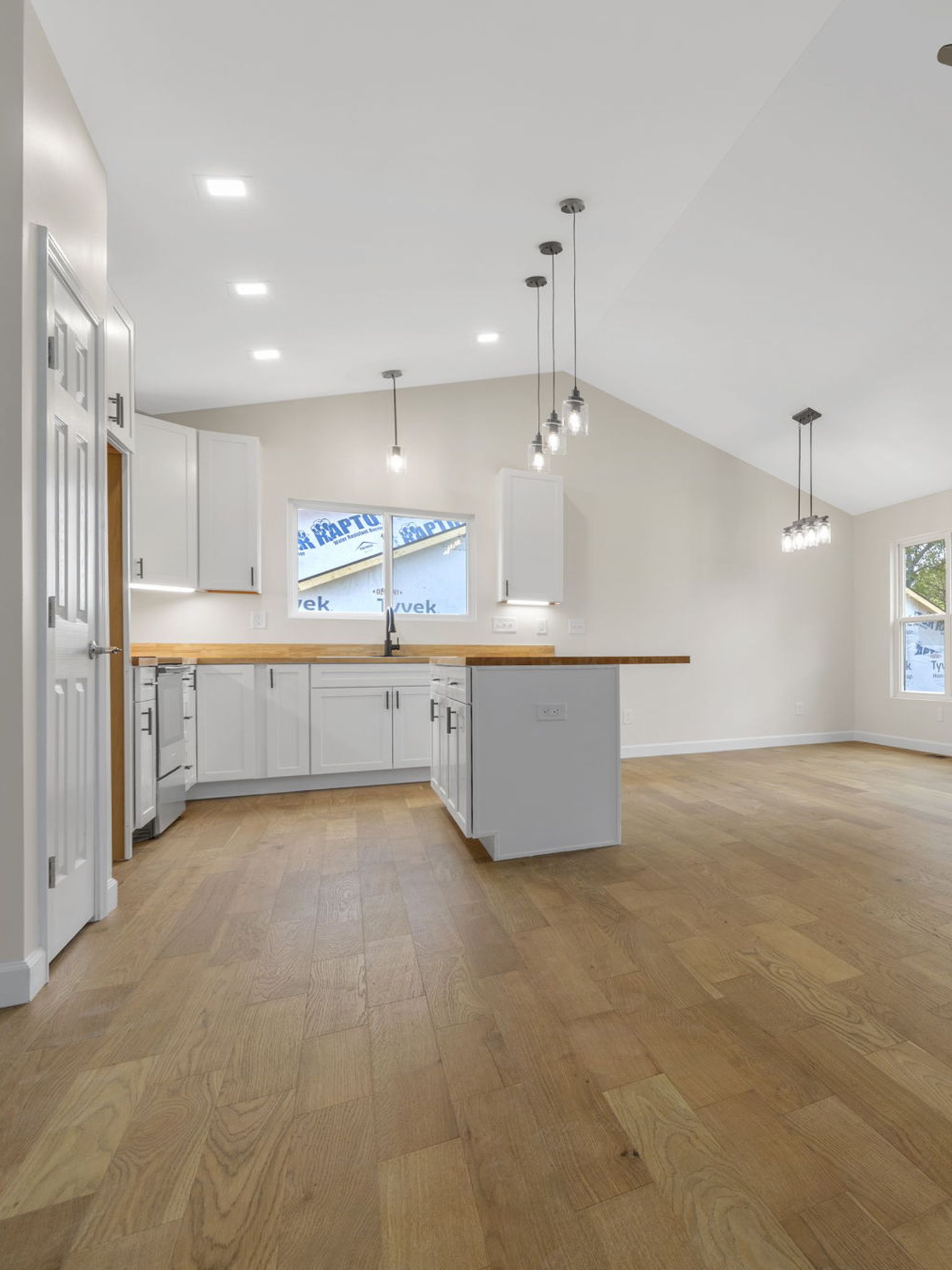 Bright empty kitchen and dining area with white cabinets, wood island, pendant lights, and hardwood floors