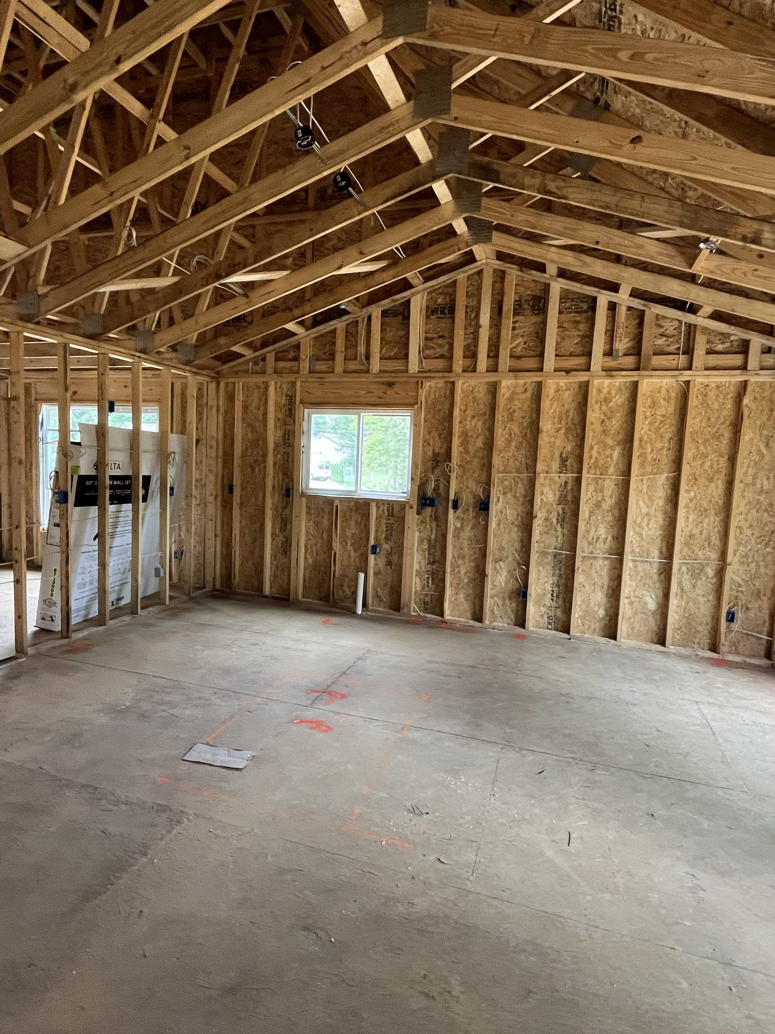 Unfinished room with exposed wooden framing, trusses, and concrete floor, lit by two windows.