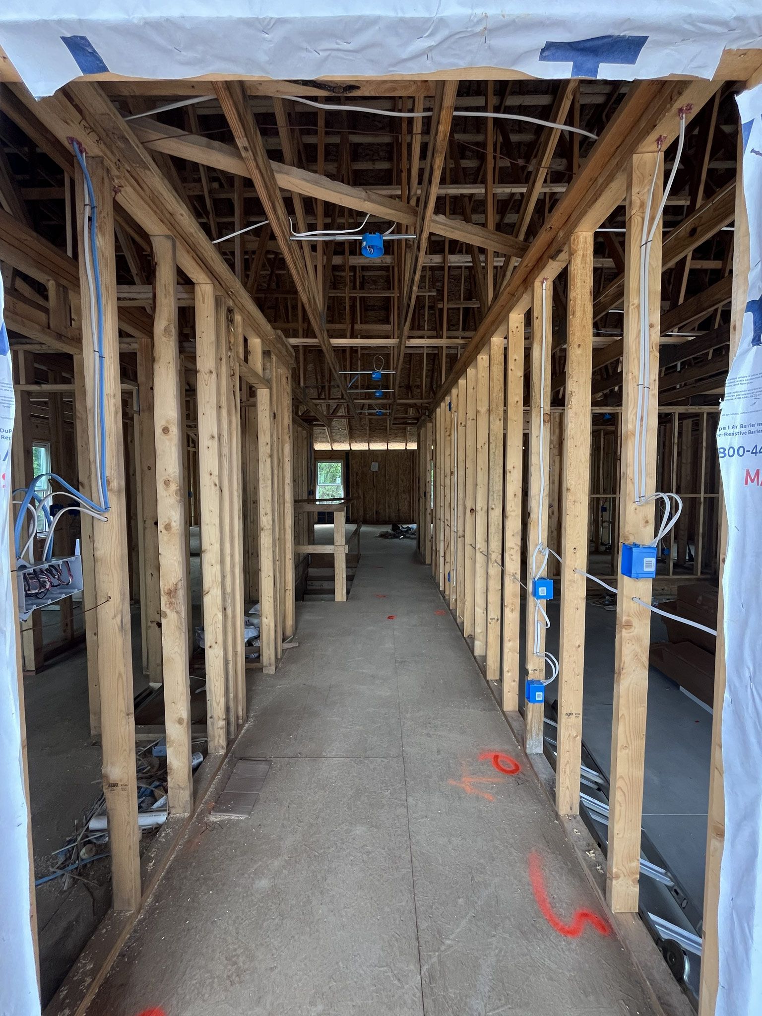 Unfinished house interior with exposed wooden framing, wiring, and a concrete floor corridor