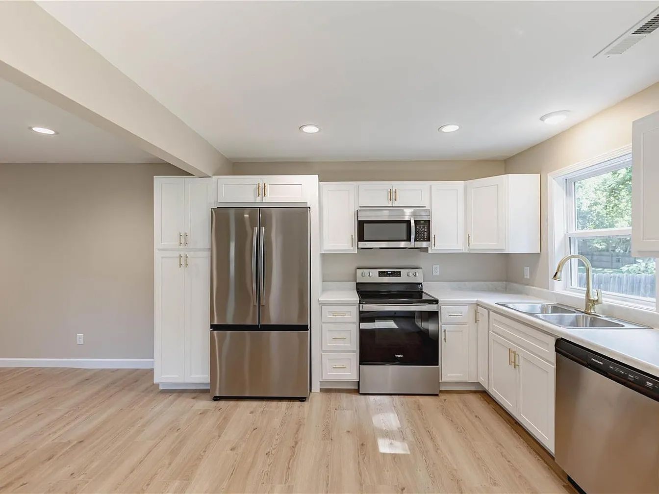 Bright modern kitchen with stainless steel appliances, white cabinets, and light wood floors
