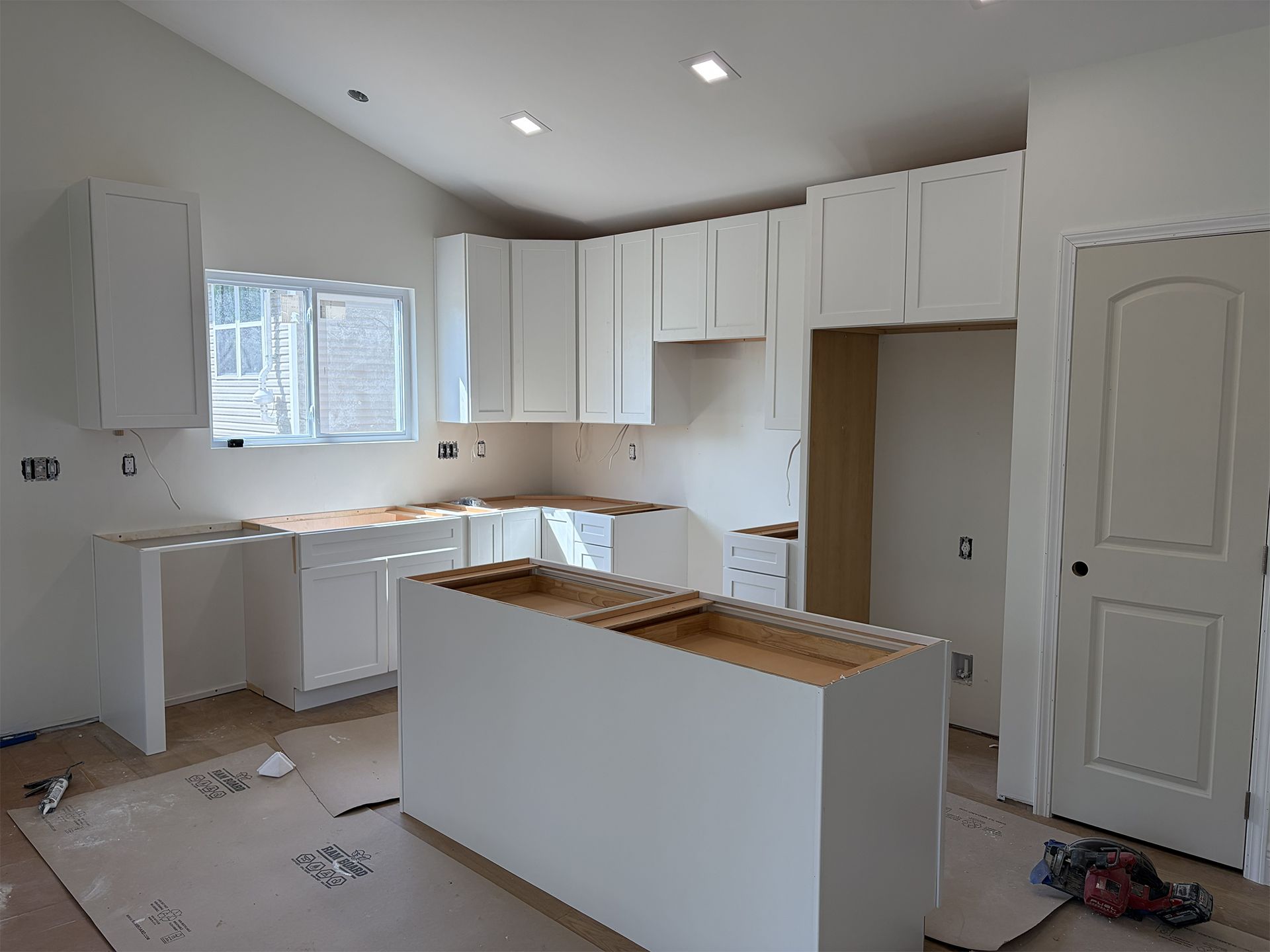 Partially finished white kitchen with cabinets, island, and cardboard on the floor