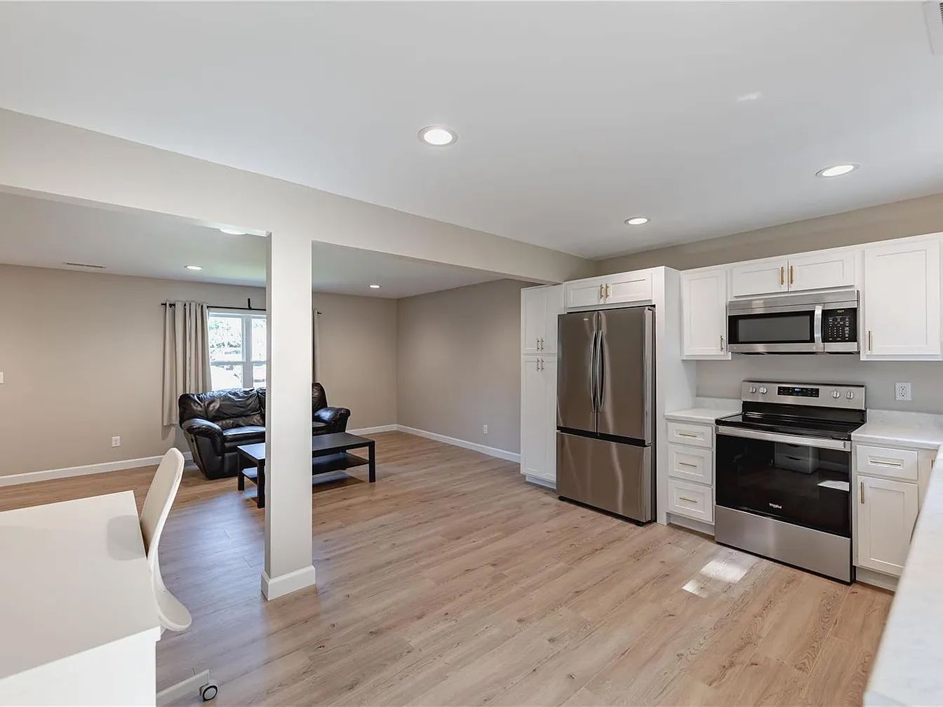 Open-plan kitchen and living room with stainless appliances, light wood floors, and recessed lighting