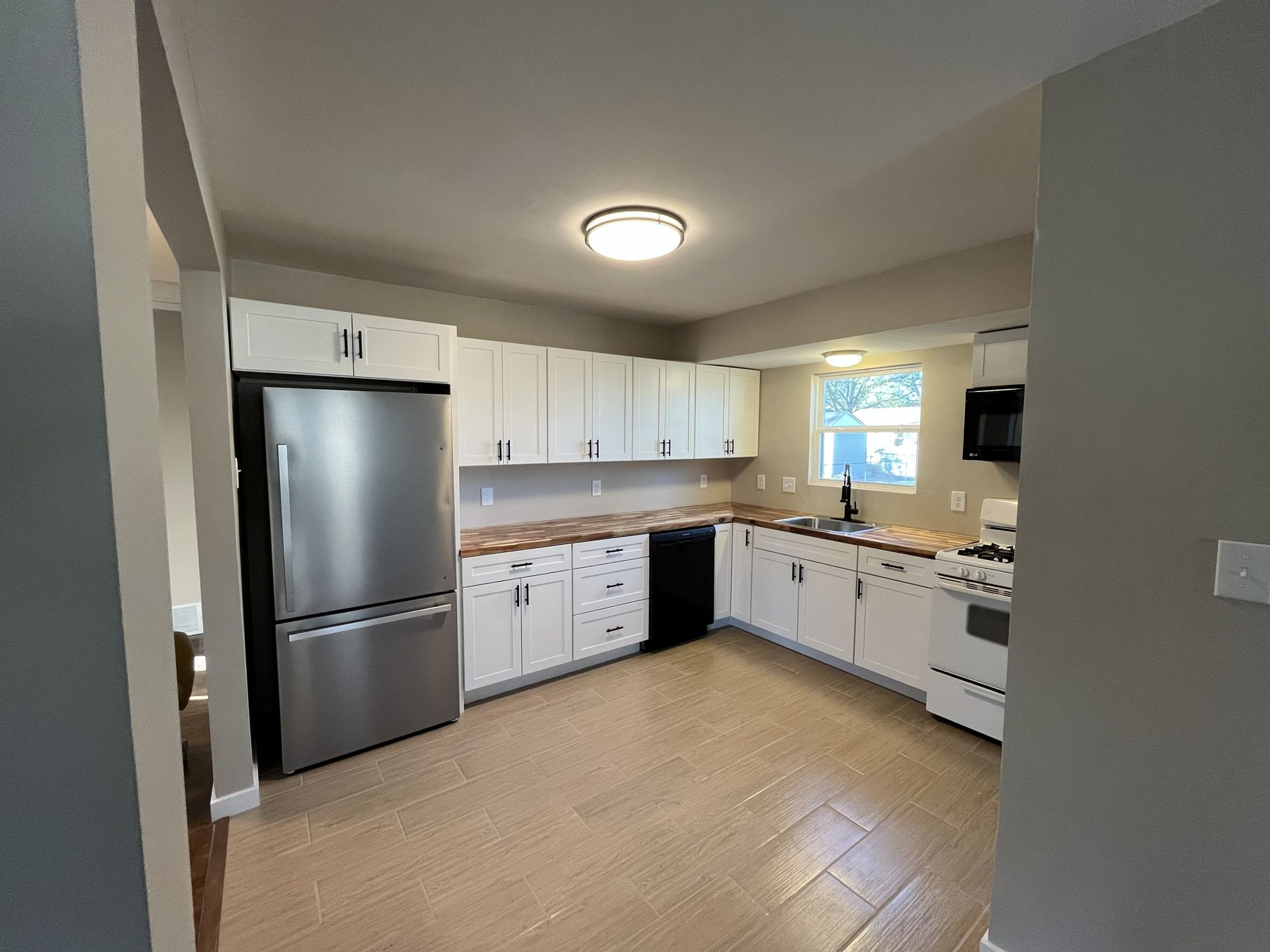 Modern kitchen with white cabinets, stainless steel fridge, beige tile floor, and a window over the sink