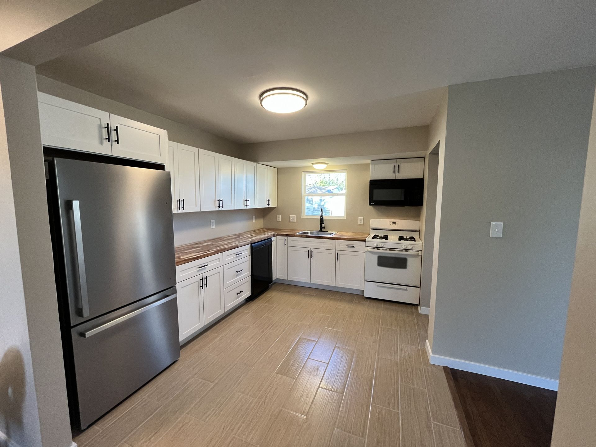 Small white kitchen with stainless fridge, white cabinets, and tan tile floor.