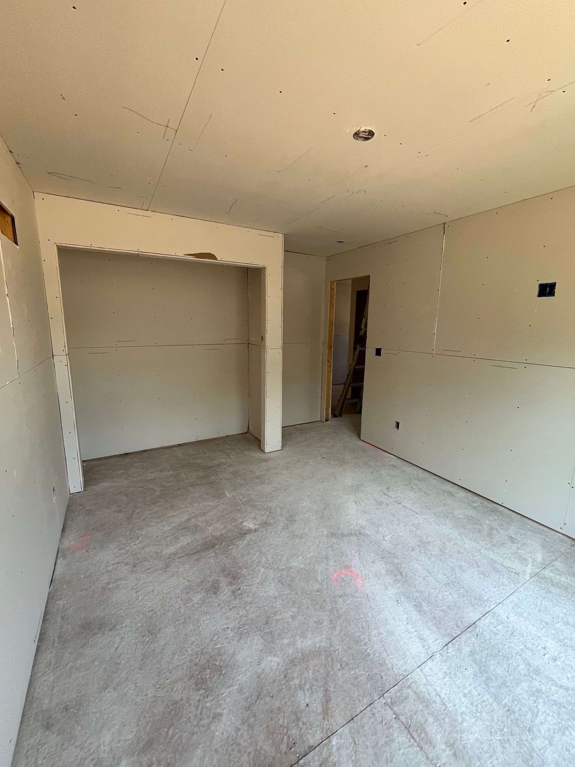 Empty unfinished room with beige walls, concrete floor, and open closet nook.