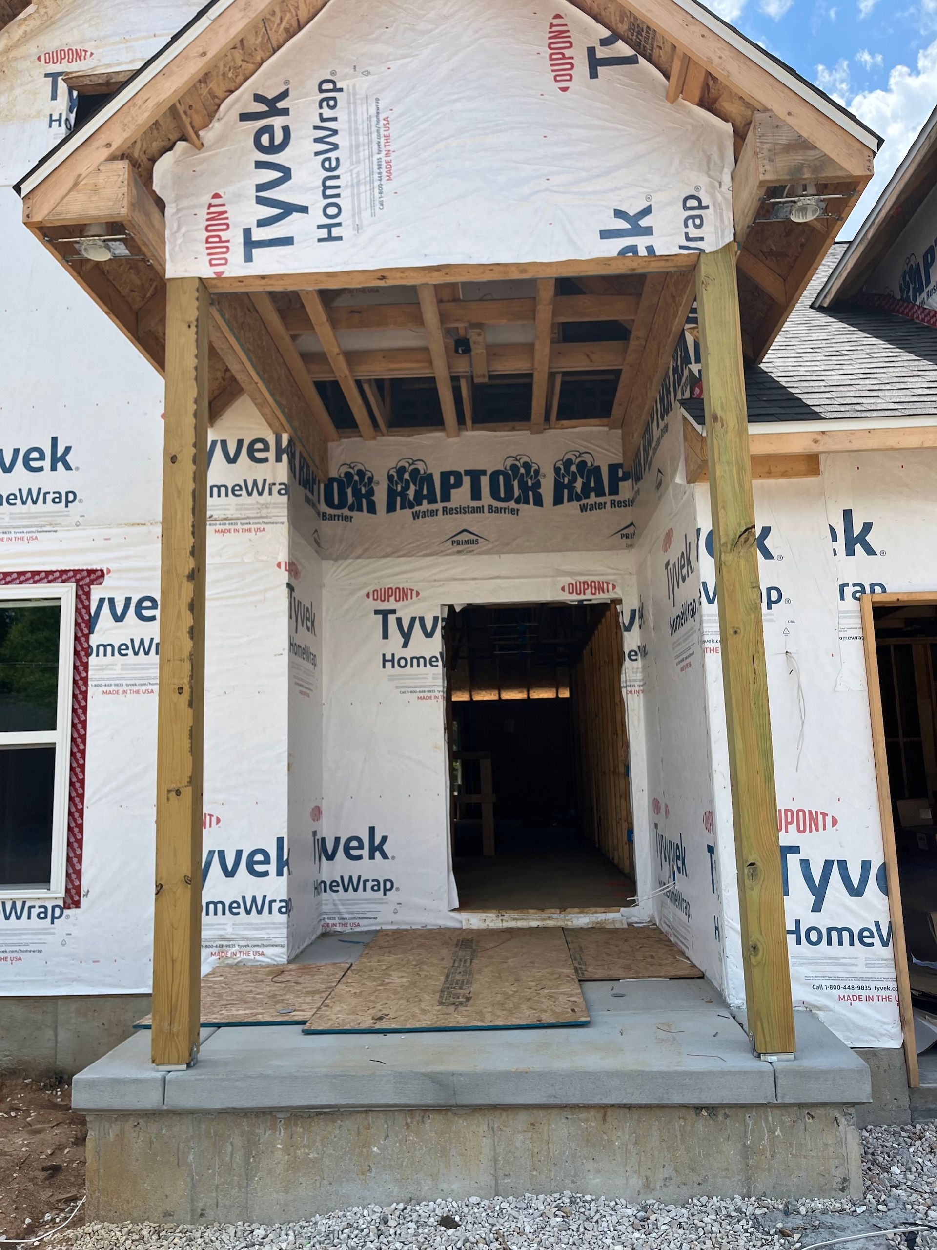 Partially built house entrance wrapped in Tyvek, with wooden framing and a concrete stoop