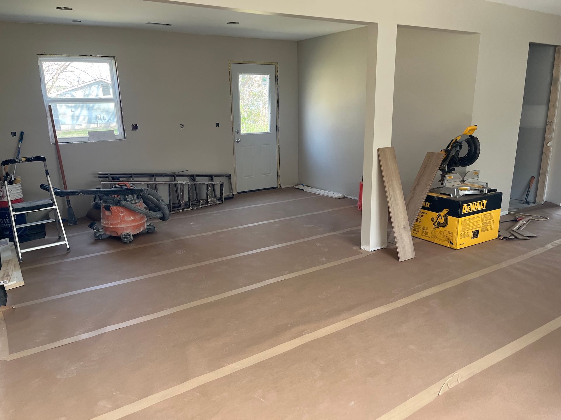 Partially renovated room with drywall, tools, and a ladder on plastic-covered floor