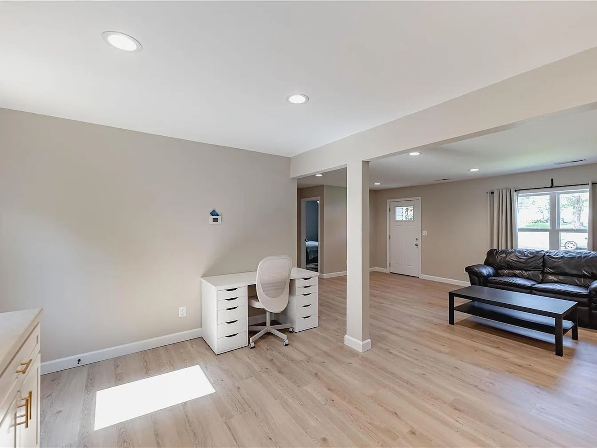 Bright empty living room with light wood floors, desk and chair, and sofa near large windows