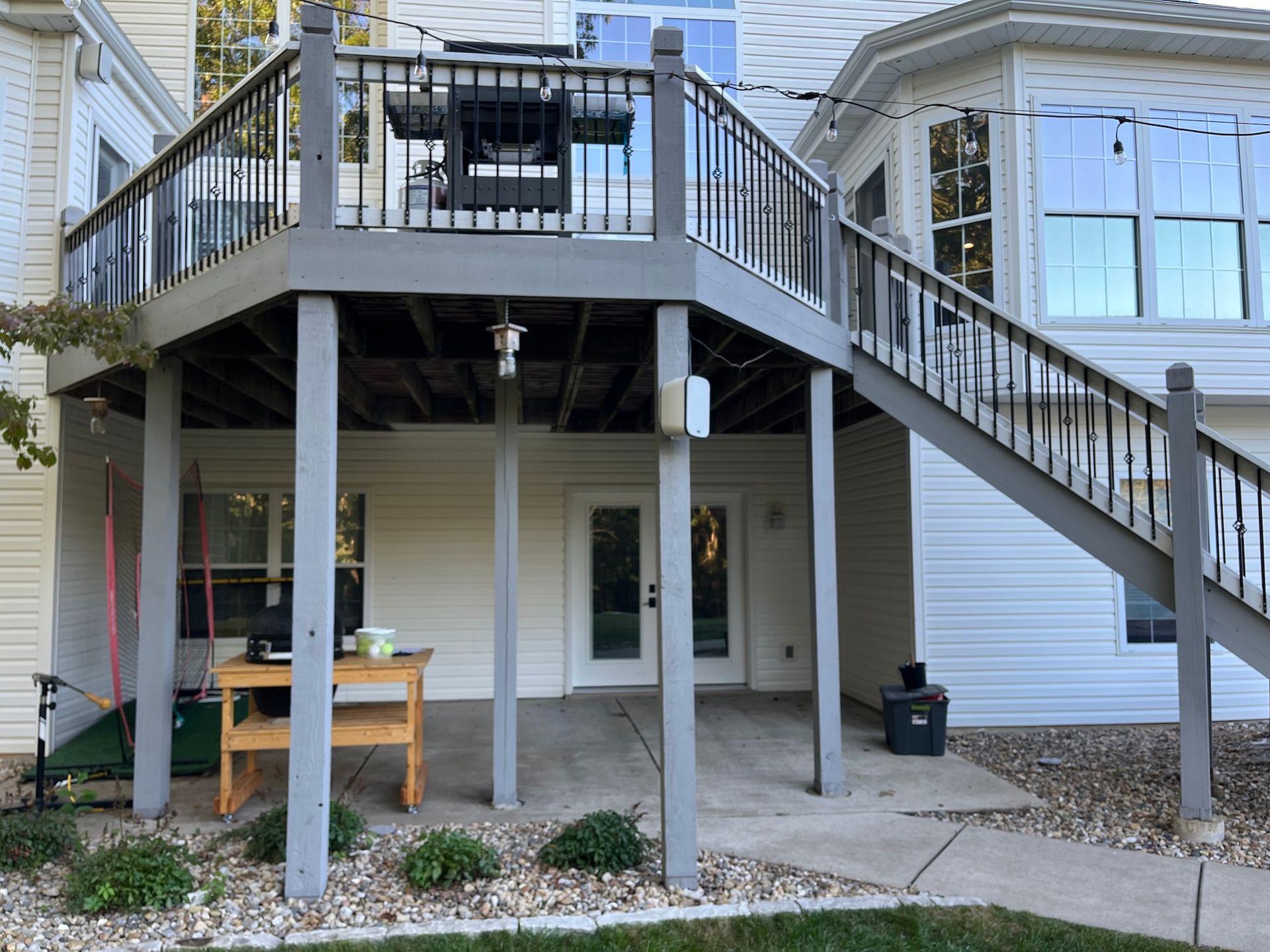 Backyard deck stairs leading to a raised patio with railing, table, and a door below.