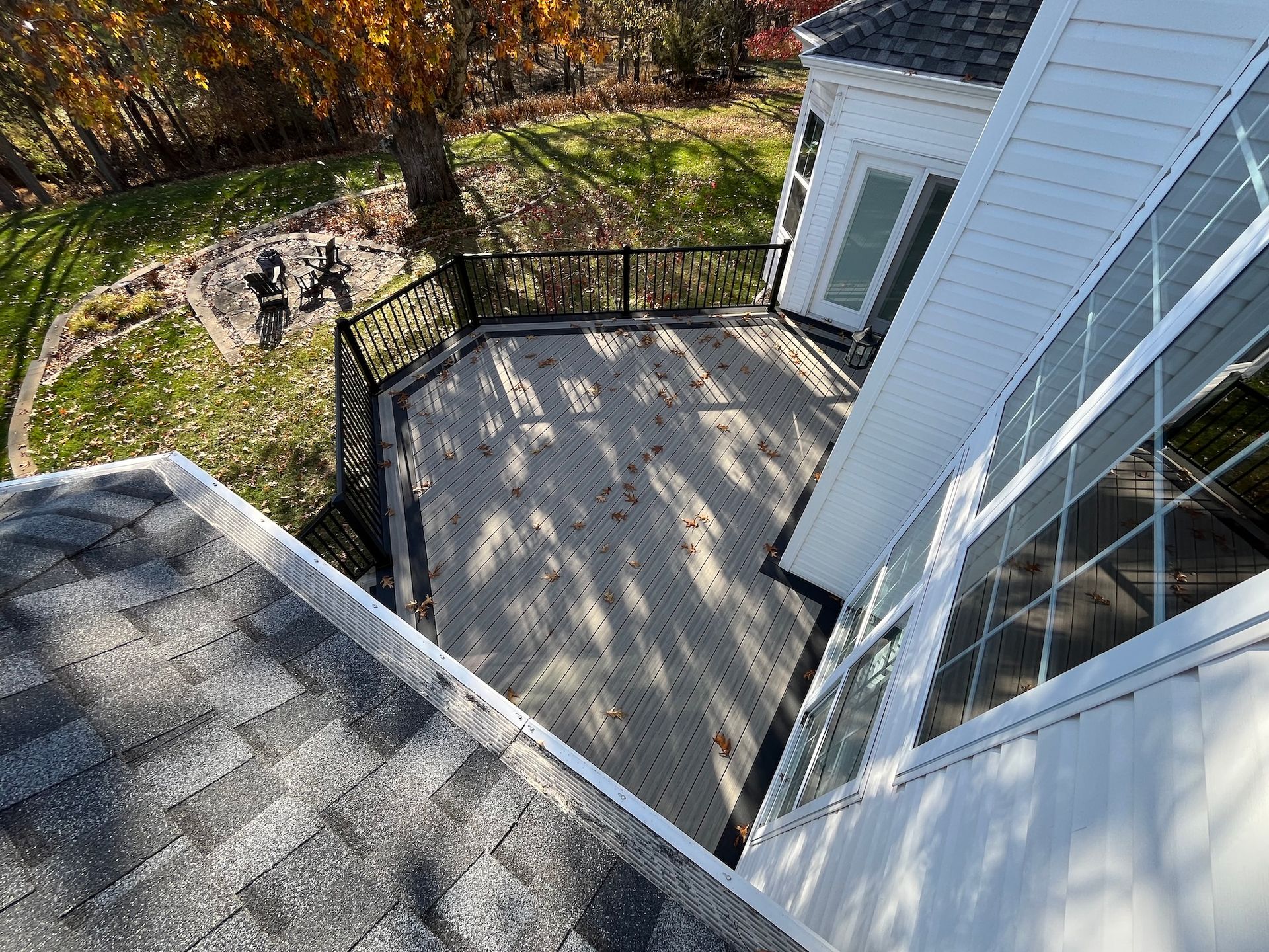 Backyard deck with black railing beside a white house, viewed from an upper roof.