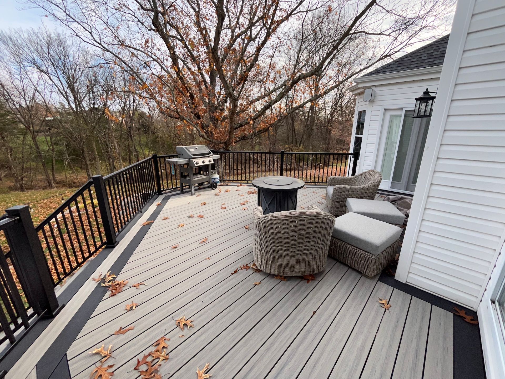 Outdoor deck with black railing, gray chairs, and a fire pit overlooking bare trees