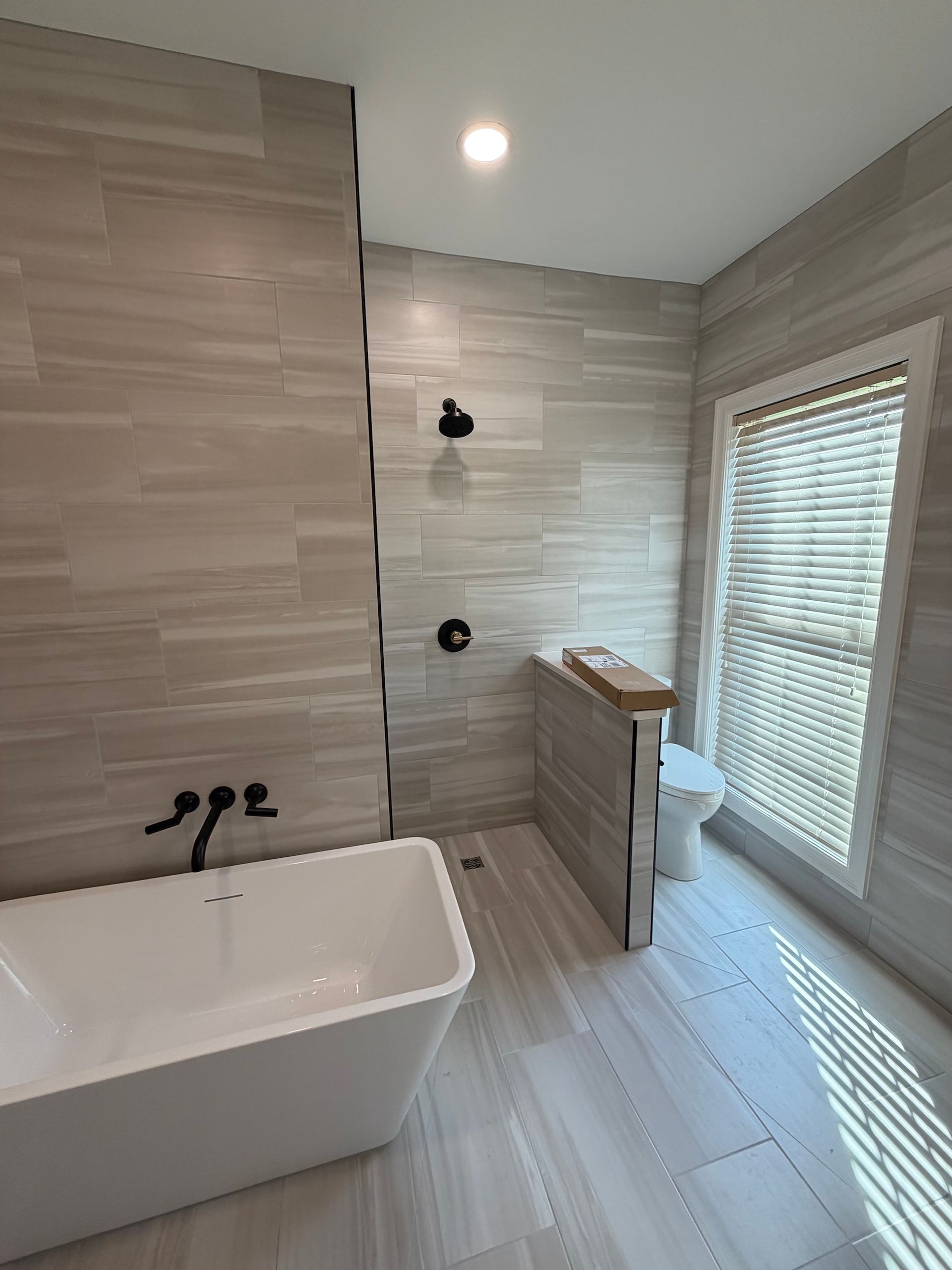 Modern bathroom with freestanding tub, walk-in shower, light tile, and window blinds
