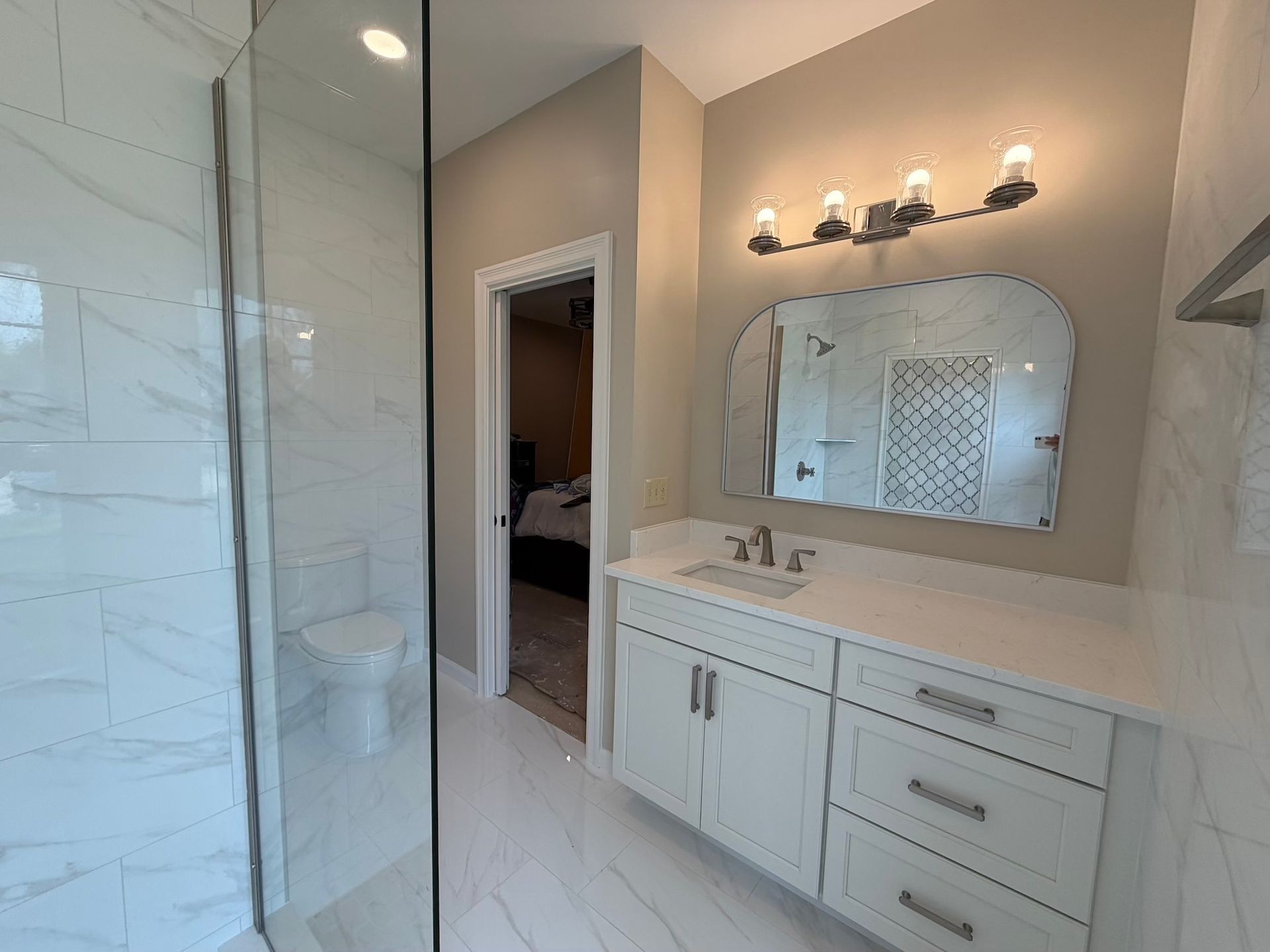 Modern bathroom with glass shower, white vanity, mirror, and wall sconces