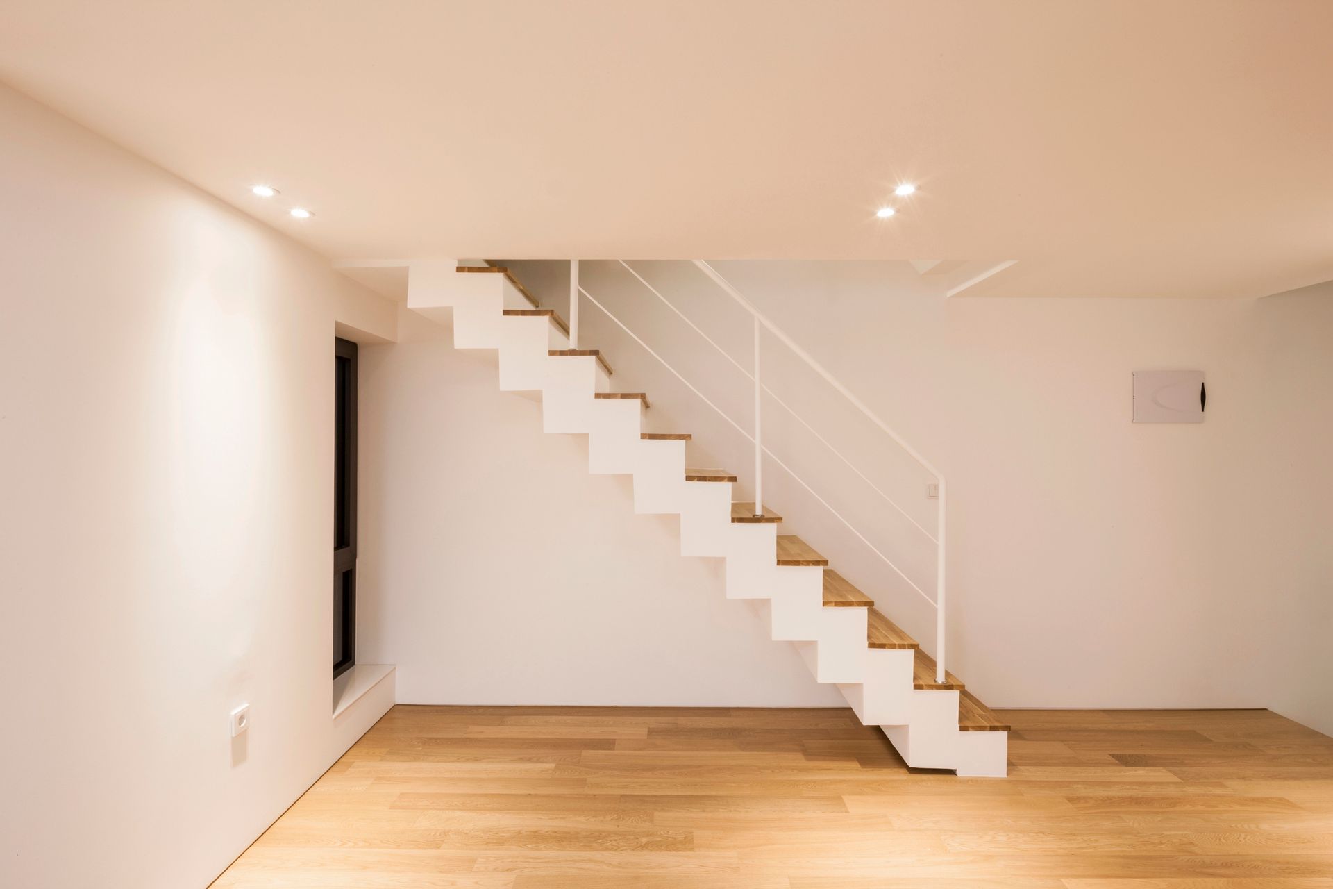Minimalist white room with a floating staircase and wooden floor