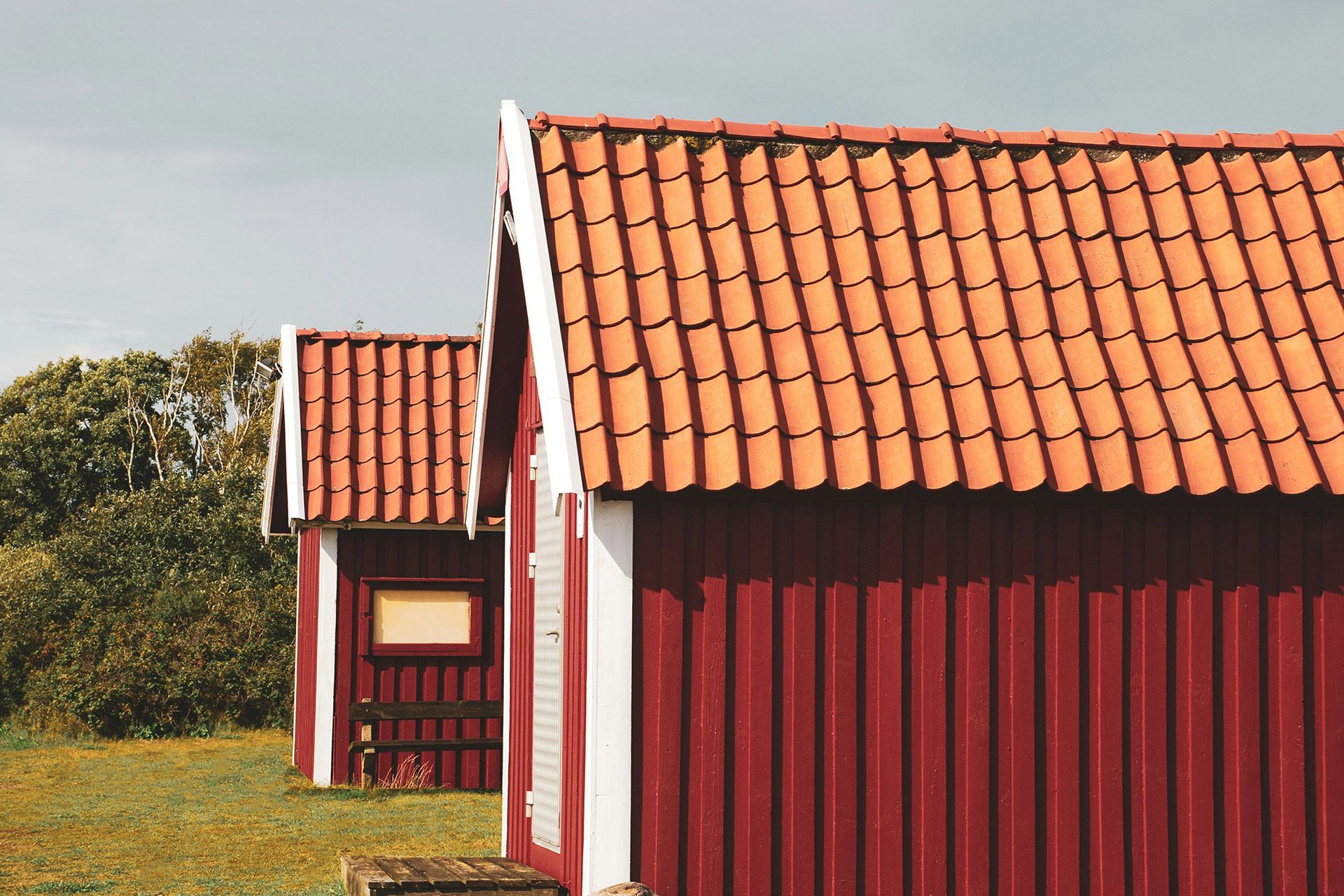Red wooden houses with orange tiled roofs in a grassy field under a pale sky