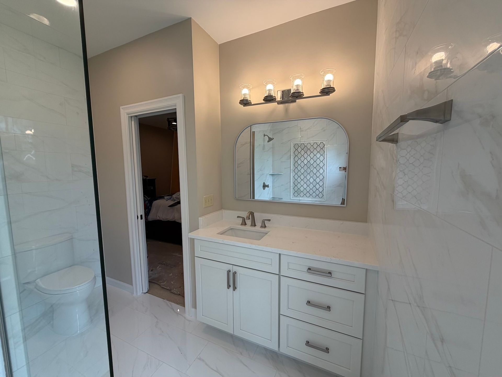 Modern bathroom with white vanity, mirror, wall sconces, and glass shower enclosure
