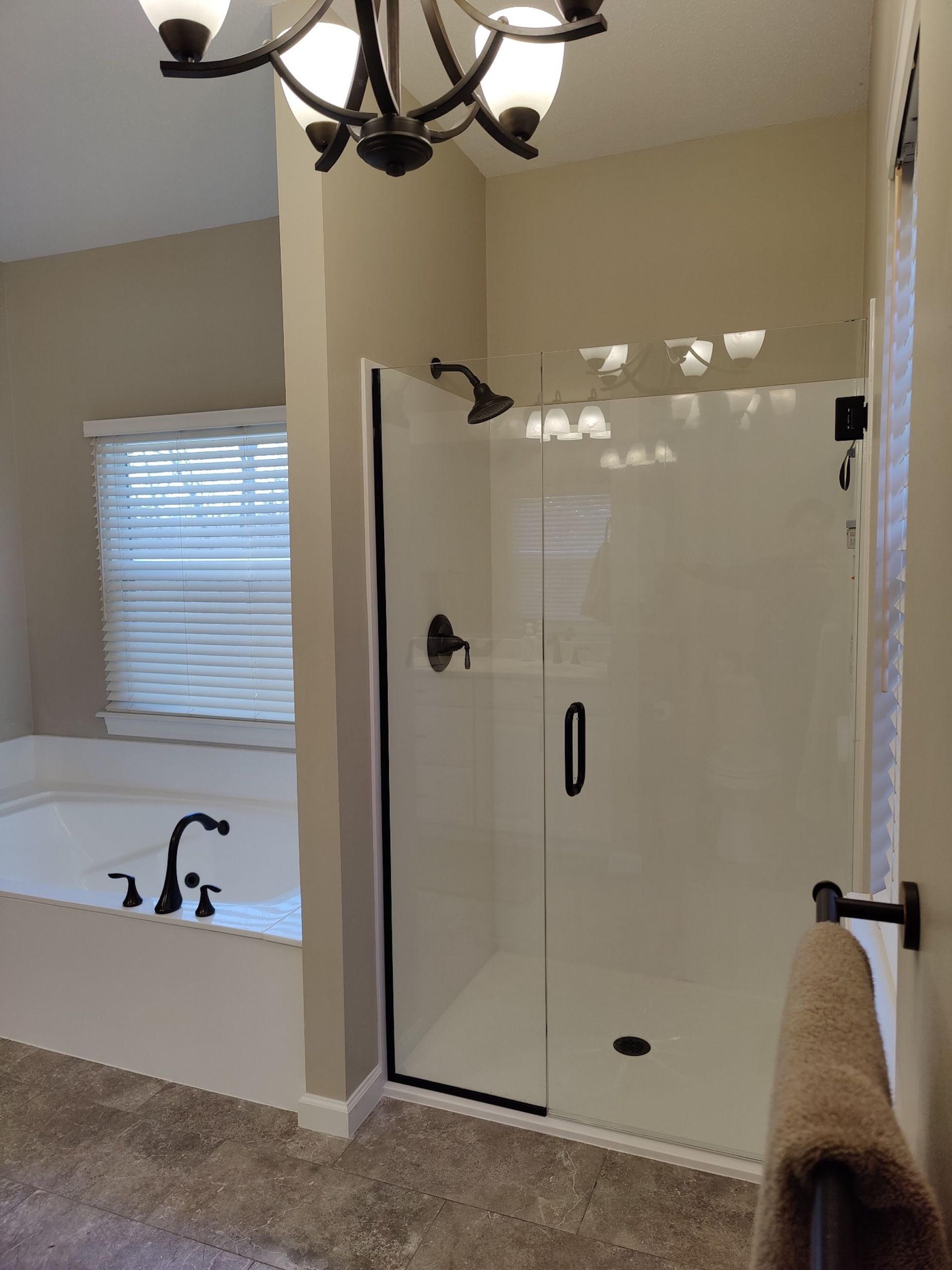 Bathroom with glass walk-in shower, soaking tub, and beige walls under a chandelier.