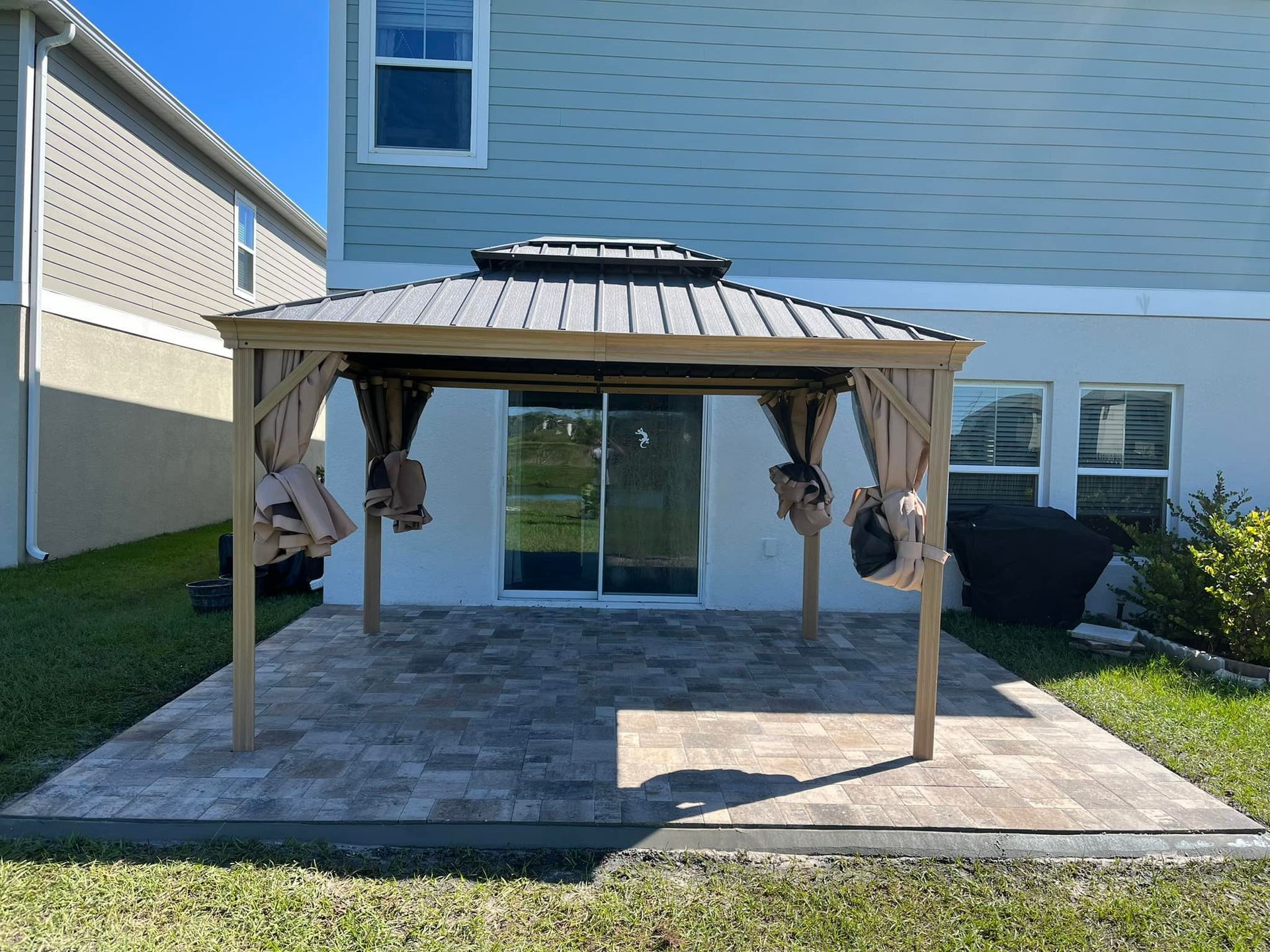 Gazebo on patio in backyard, next to a house with sliding glass door.