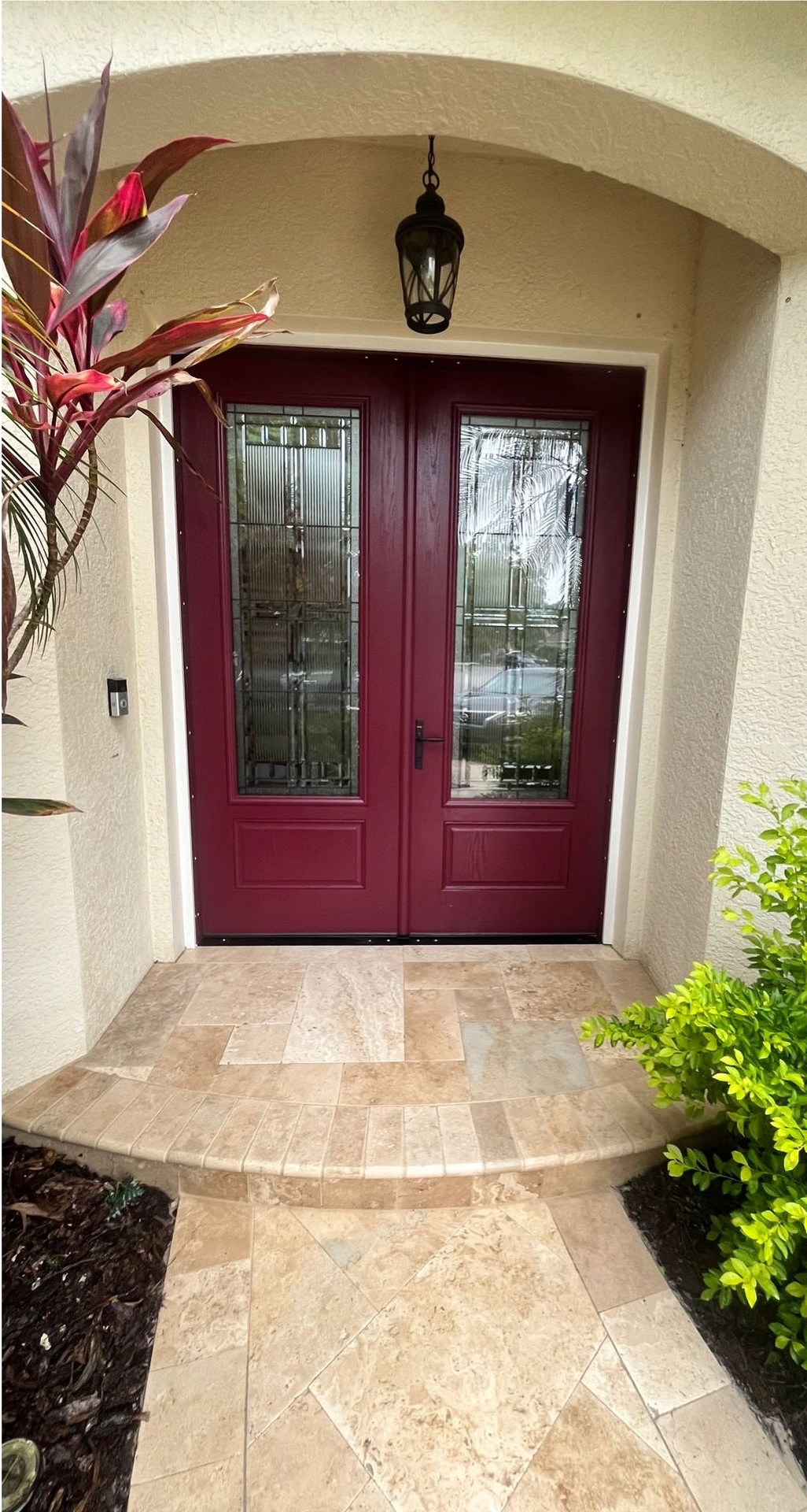 Burgundy double doors with glass panels, tan tiled entryway, and hanging lantern.