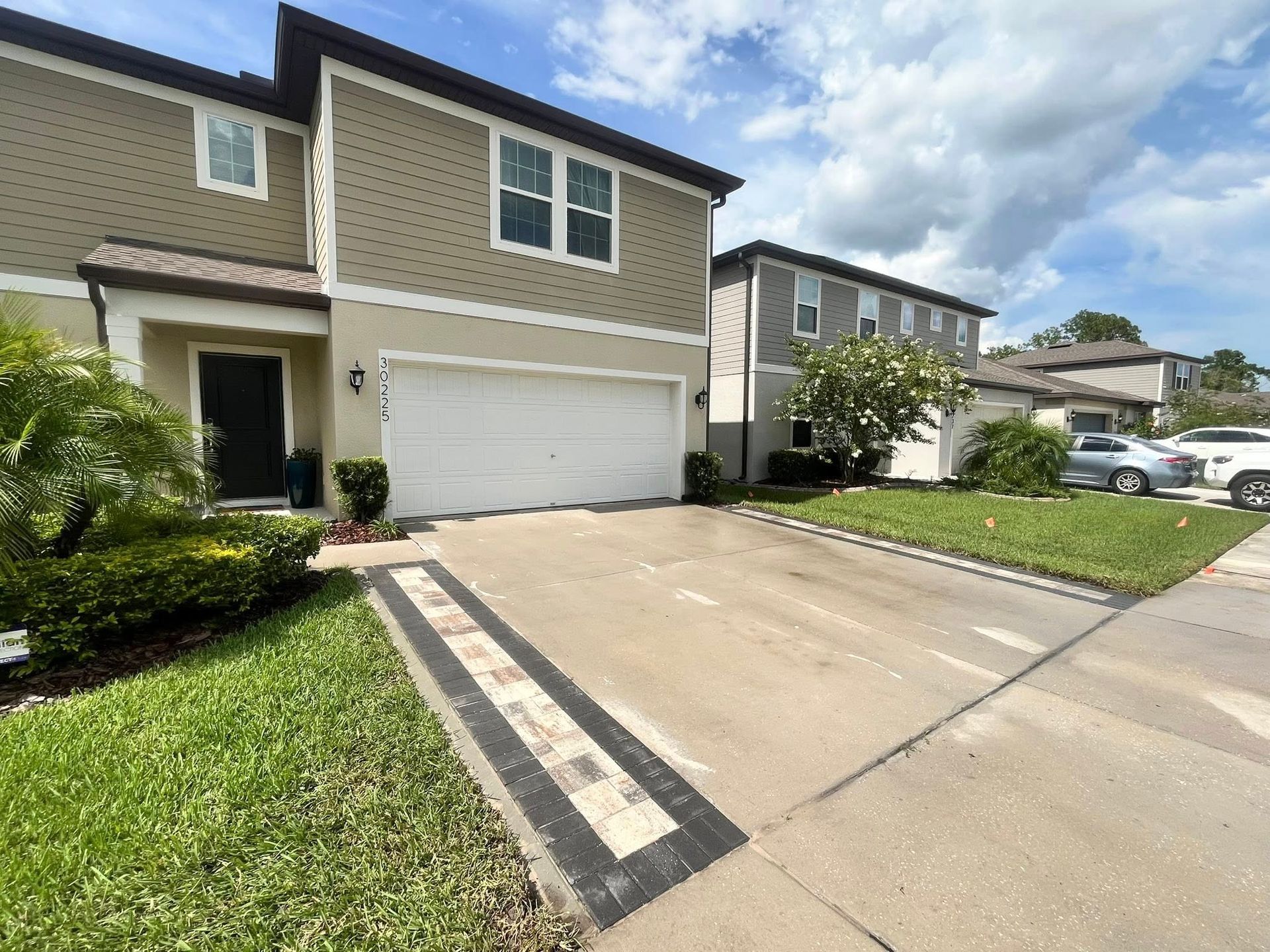 Townhouse with a driveway bordered by brick pavers and green grass.