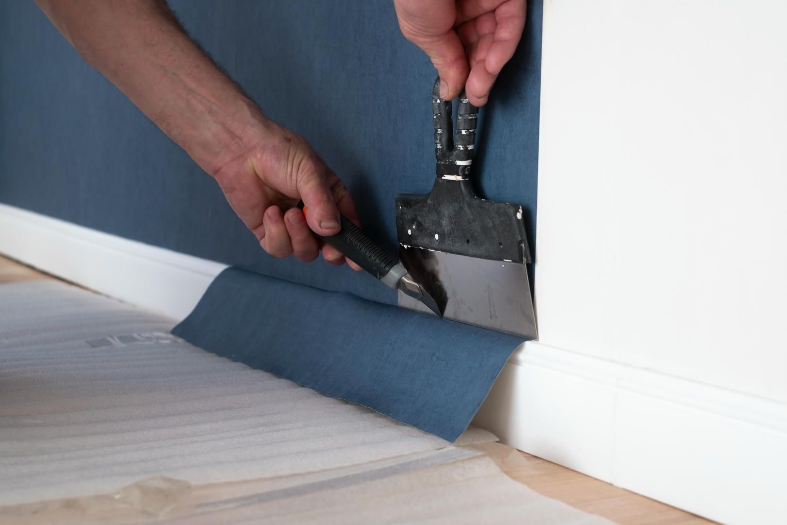 A person is removing wallpaper from a wall with a spatula.