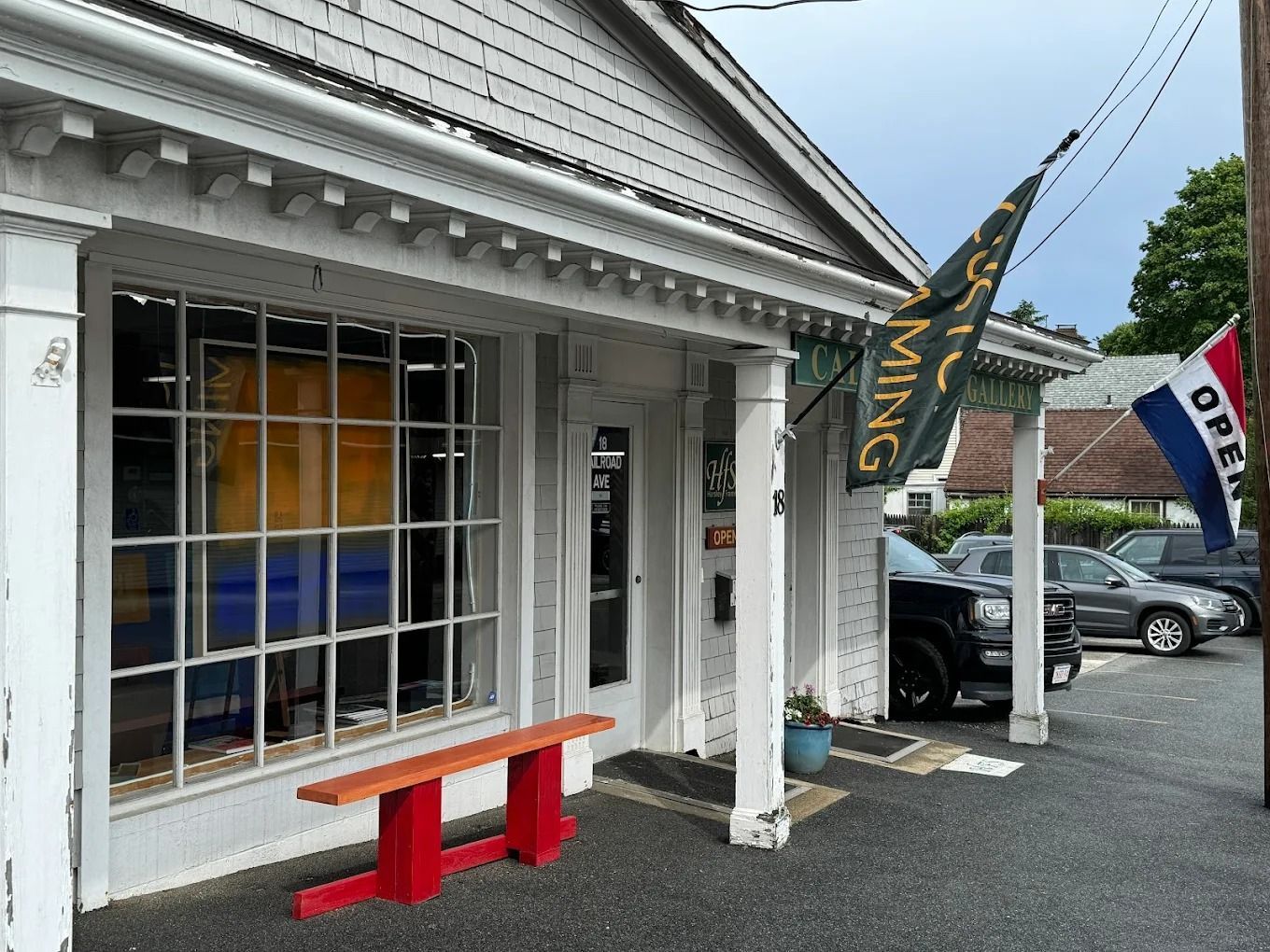 A white storefront with a large grid window, a bright red bench in front, and an
