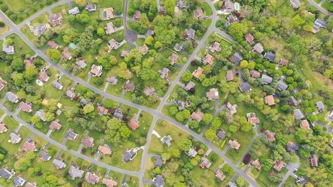 Aerial view of a leafy suburban neighborhood with winding roads and scattered houses in spring greenery