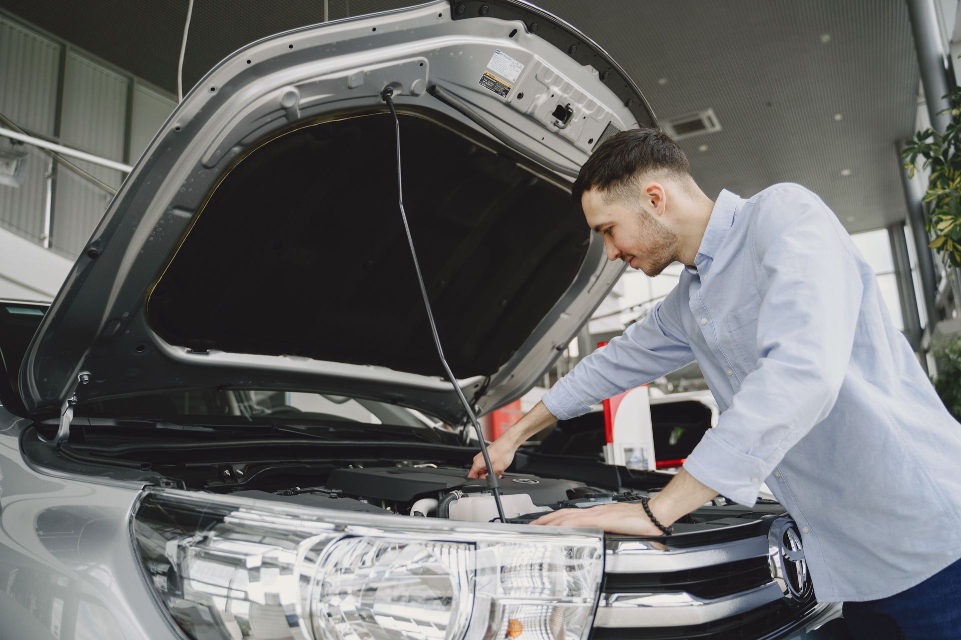 Mechanic checking engine under open hood of black car in a service garage